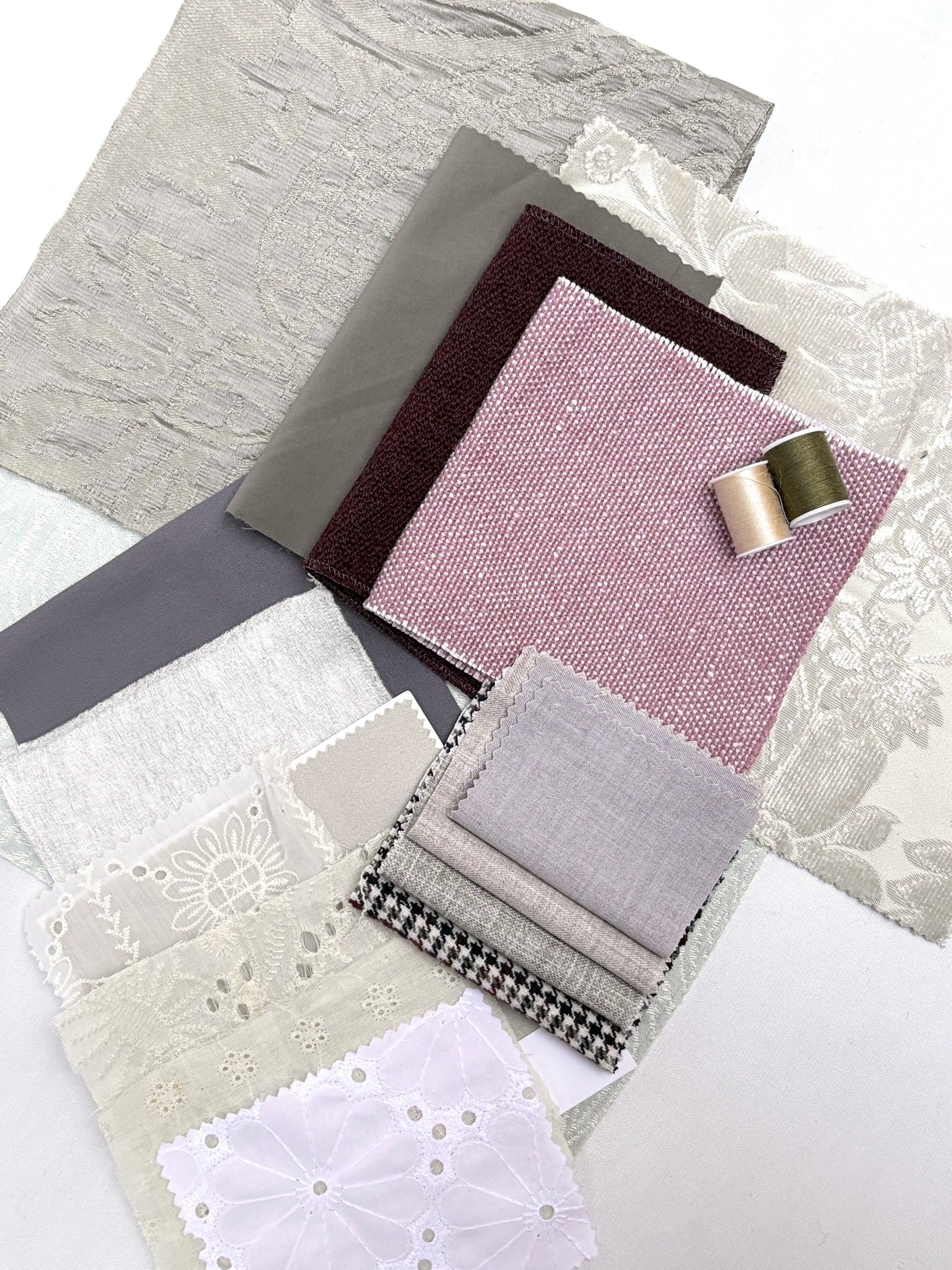 Soft neutral fabric samples layered with lace trims and coordinating thread spools.