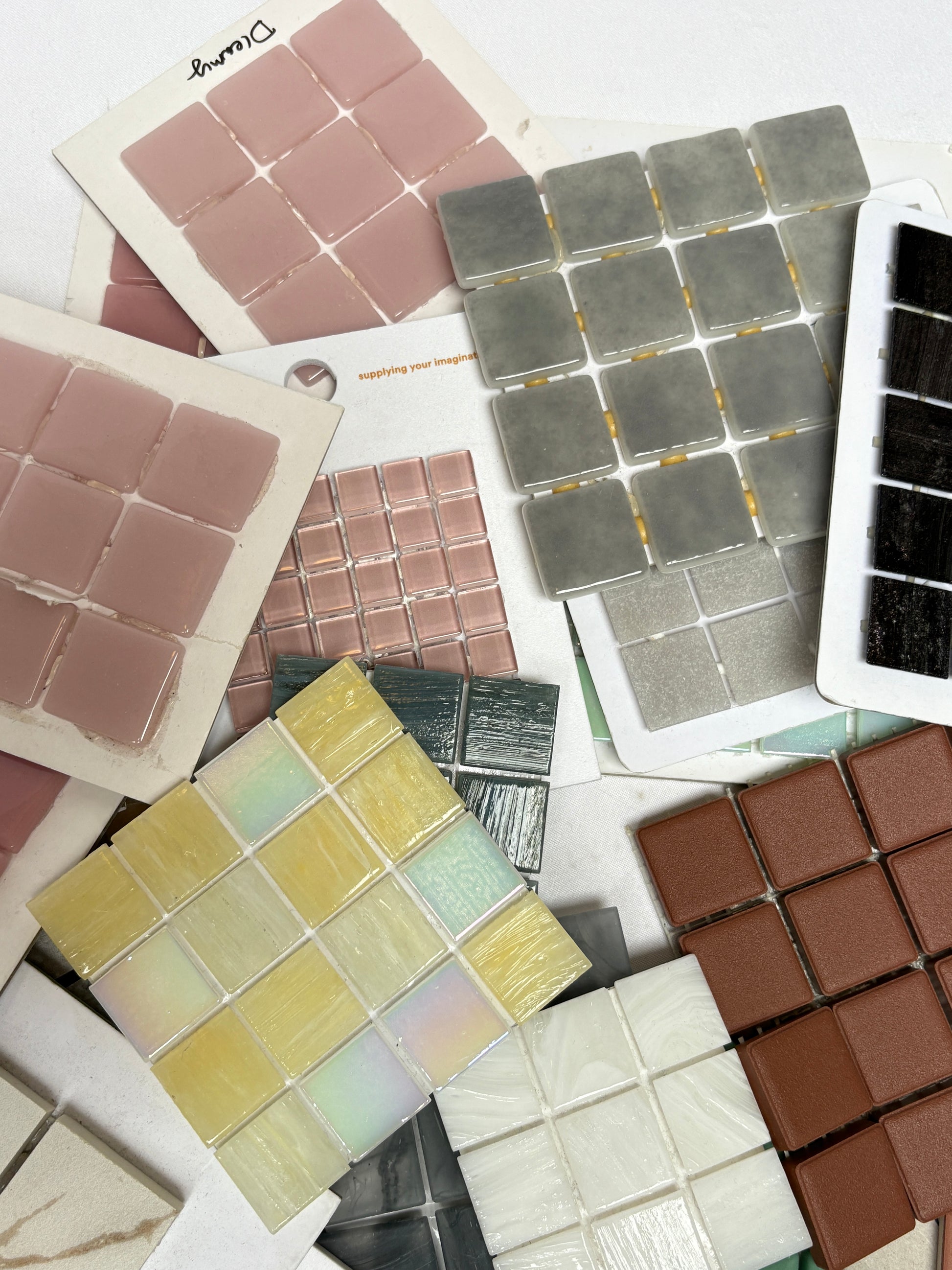 Tile sample sheets in pink, green, brown, and grey are layered together