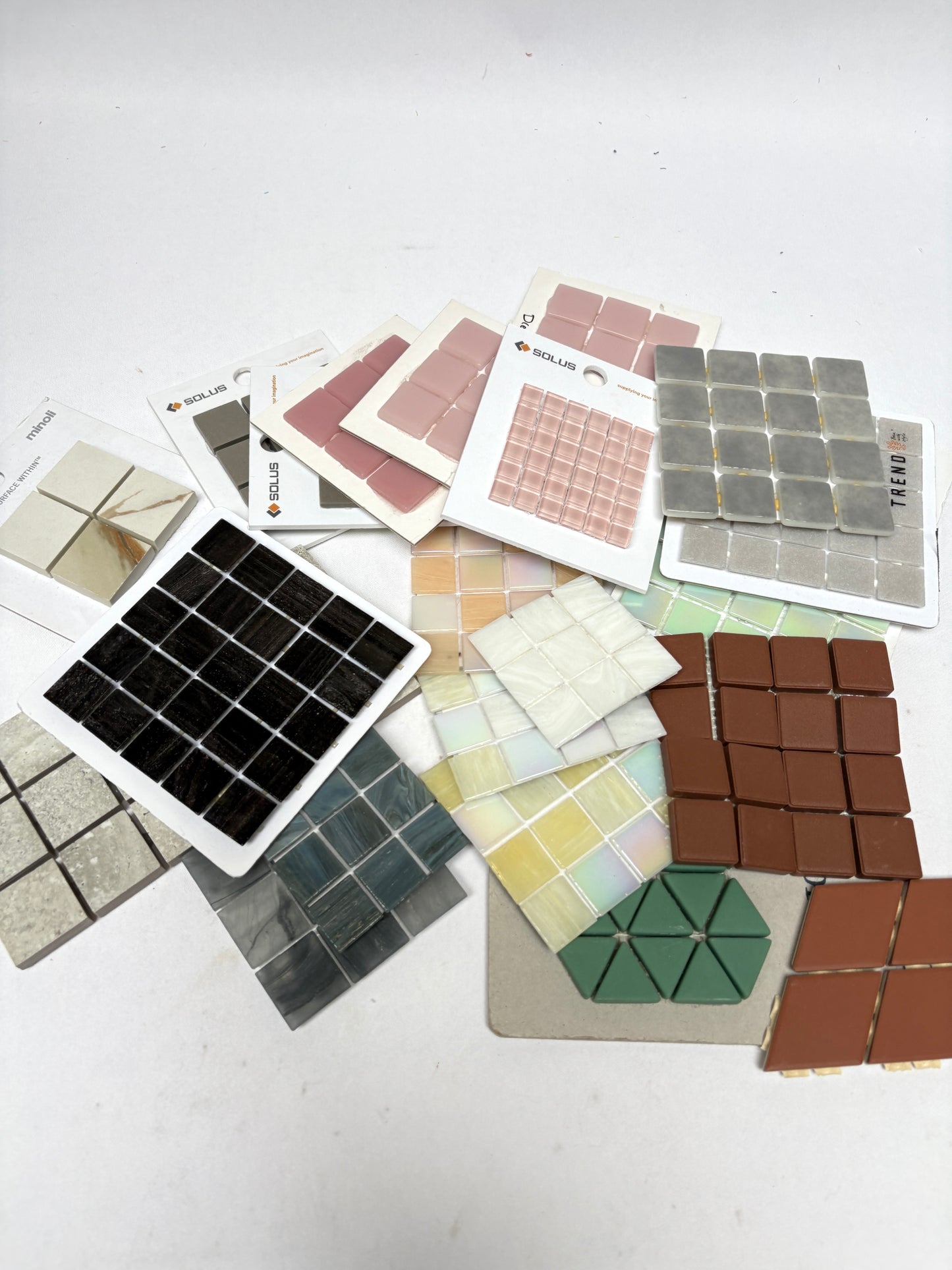 Tile sample sheets in pink, green, brown, and grey are layered together