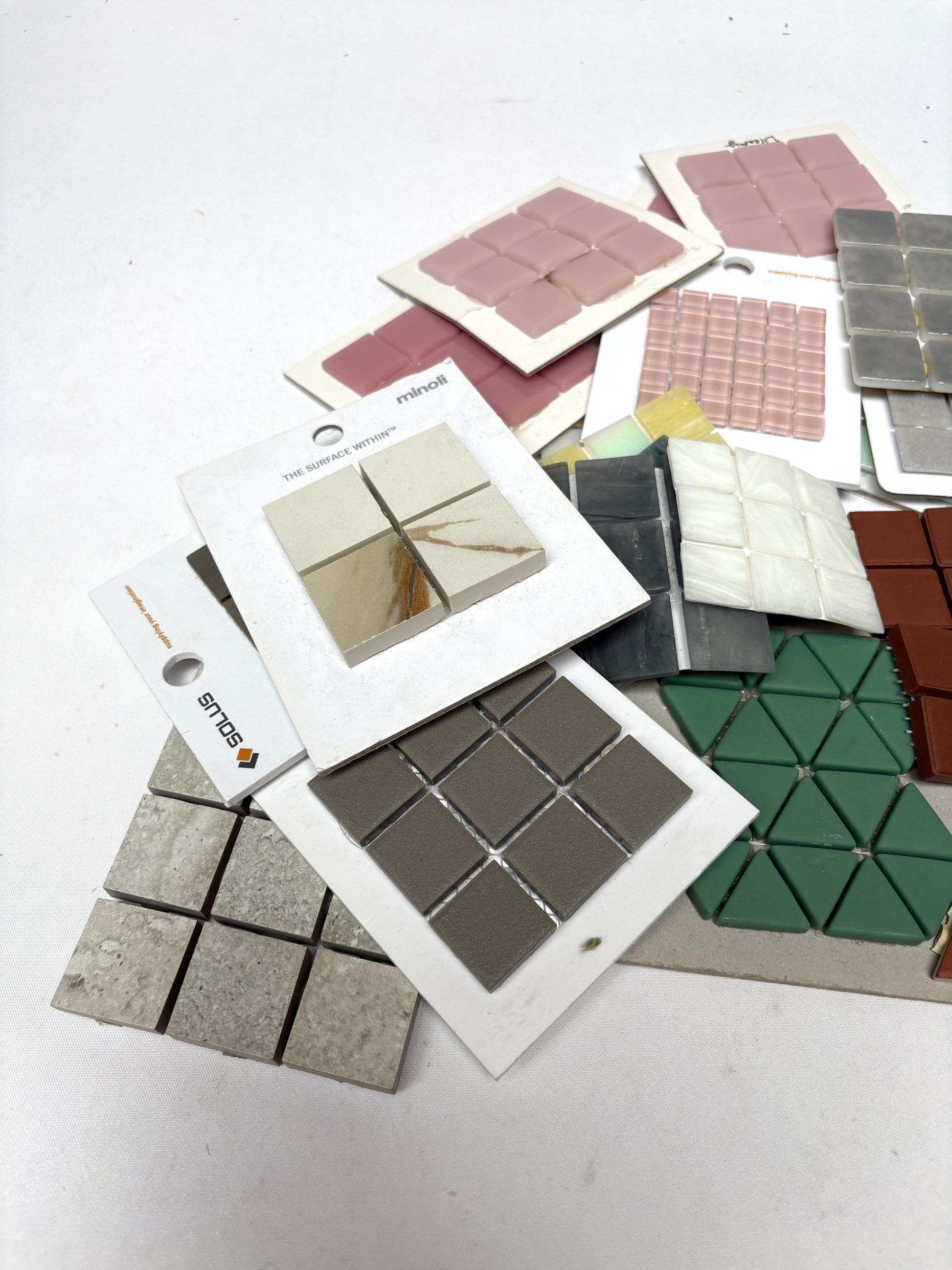 Mixed mosaic tile sheets are arranged in overlapping layers on white