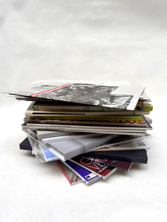 Mixed books, magazines, and paper items are stacked on white