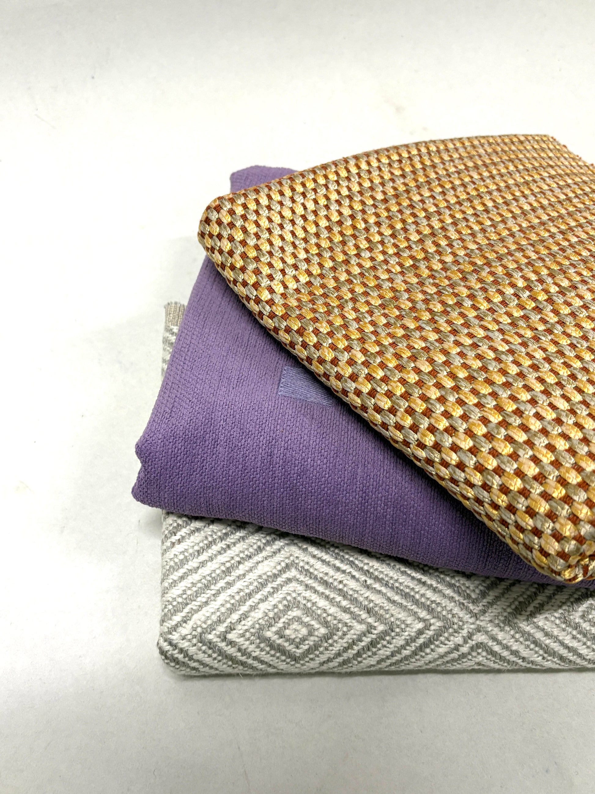 Stack of three geometric patterned fabric in purple, gold, and grey 