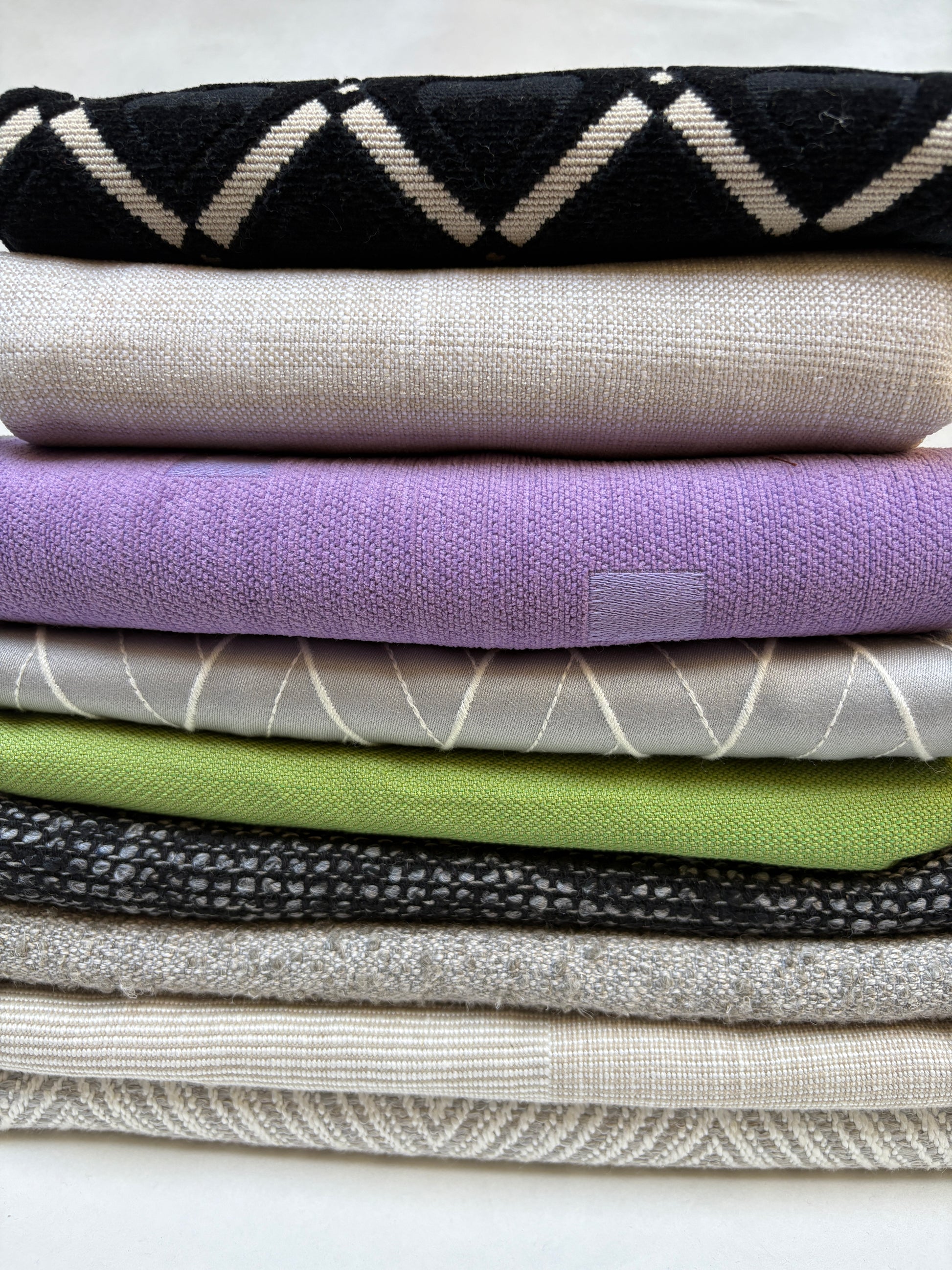 Mixed bundle of medium patterned upholstery fabric pieces stacked on white.