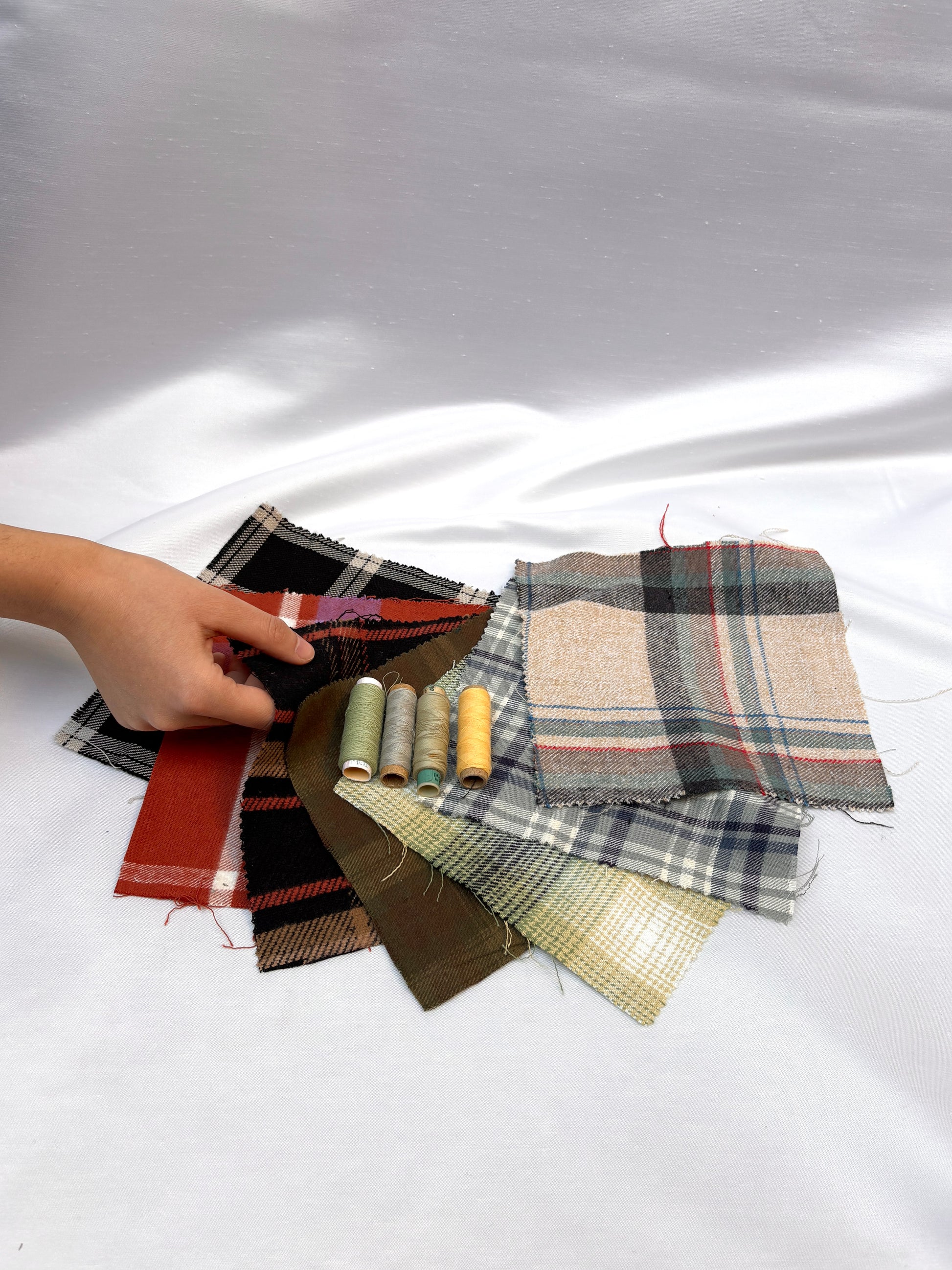 Hand holding checked fabric swatches with coordinating thread spools.