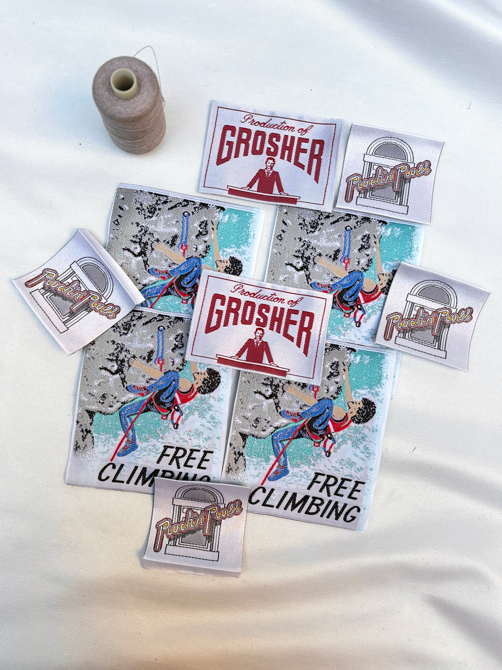 Woven labels and free climbing badges arranged with a spool of thread.