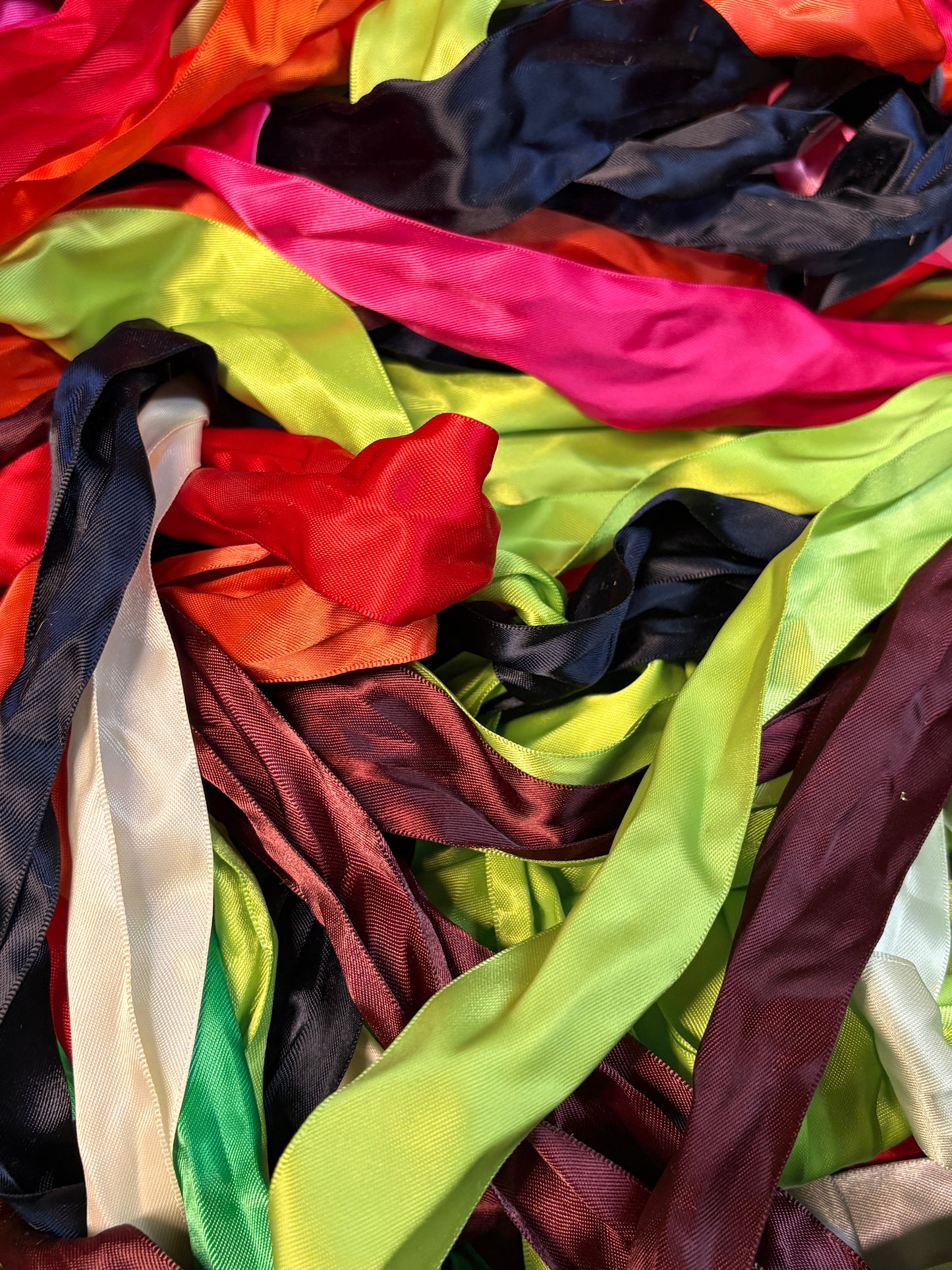 Assorted satin ribbon strips in bright colours layered in a textured pile.