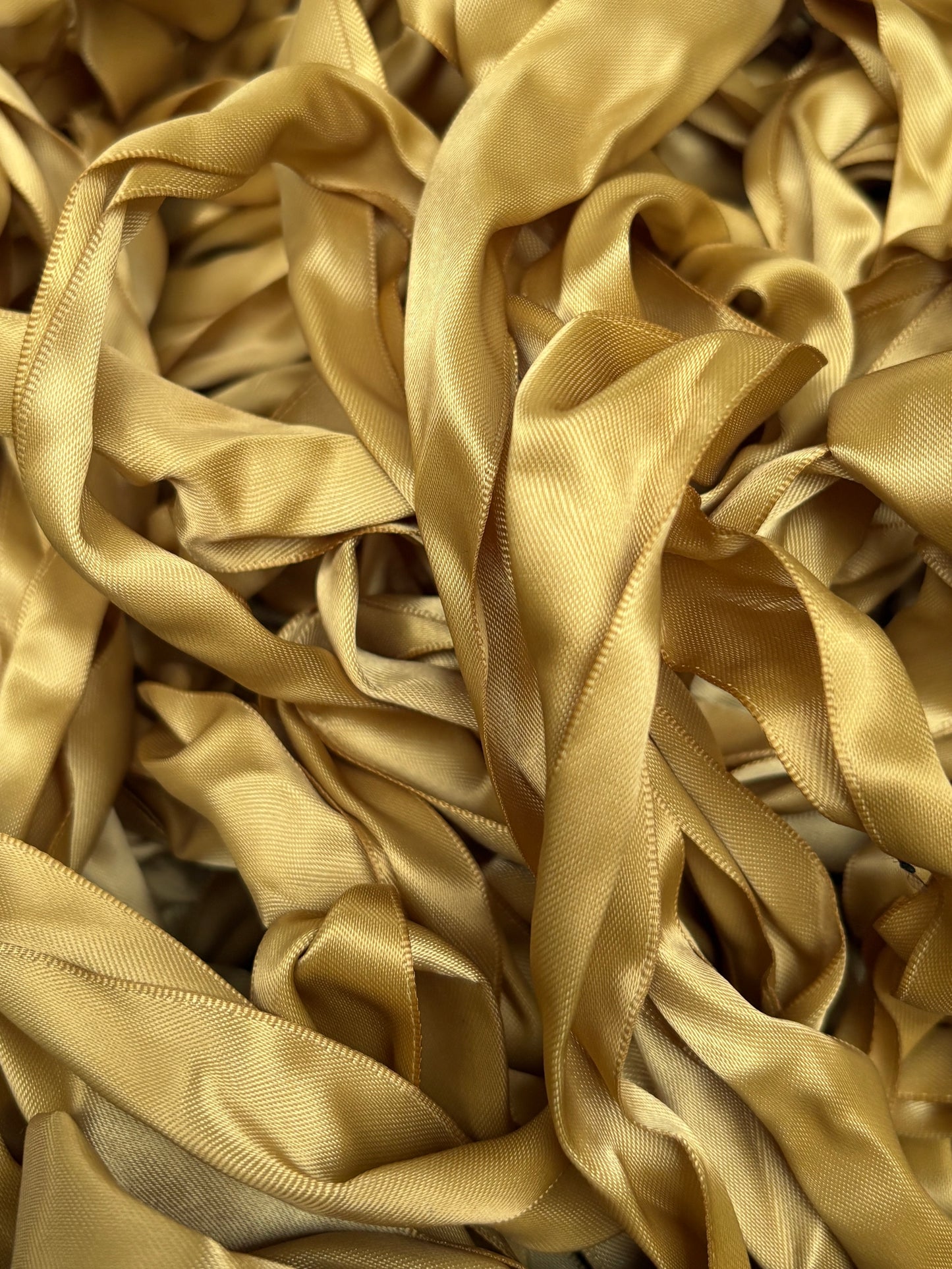 Gold satin ribbons piled together in a layered, textured arrangement.