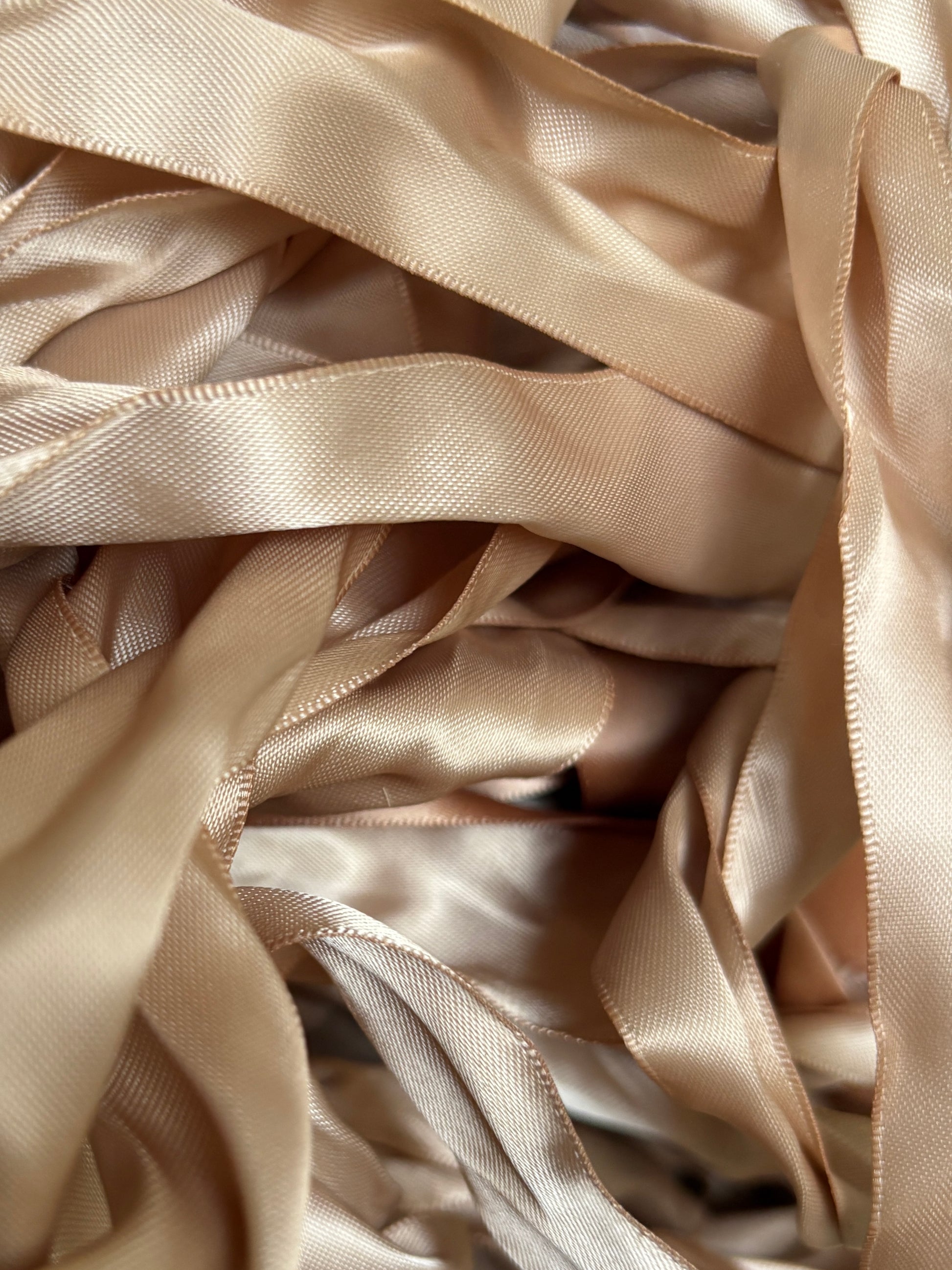A pile of champagne satin ribbons layered in soft folds.
