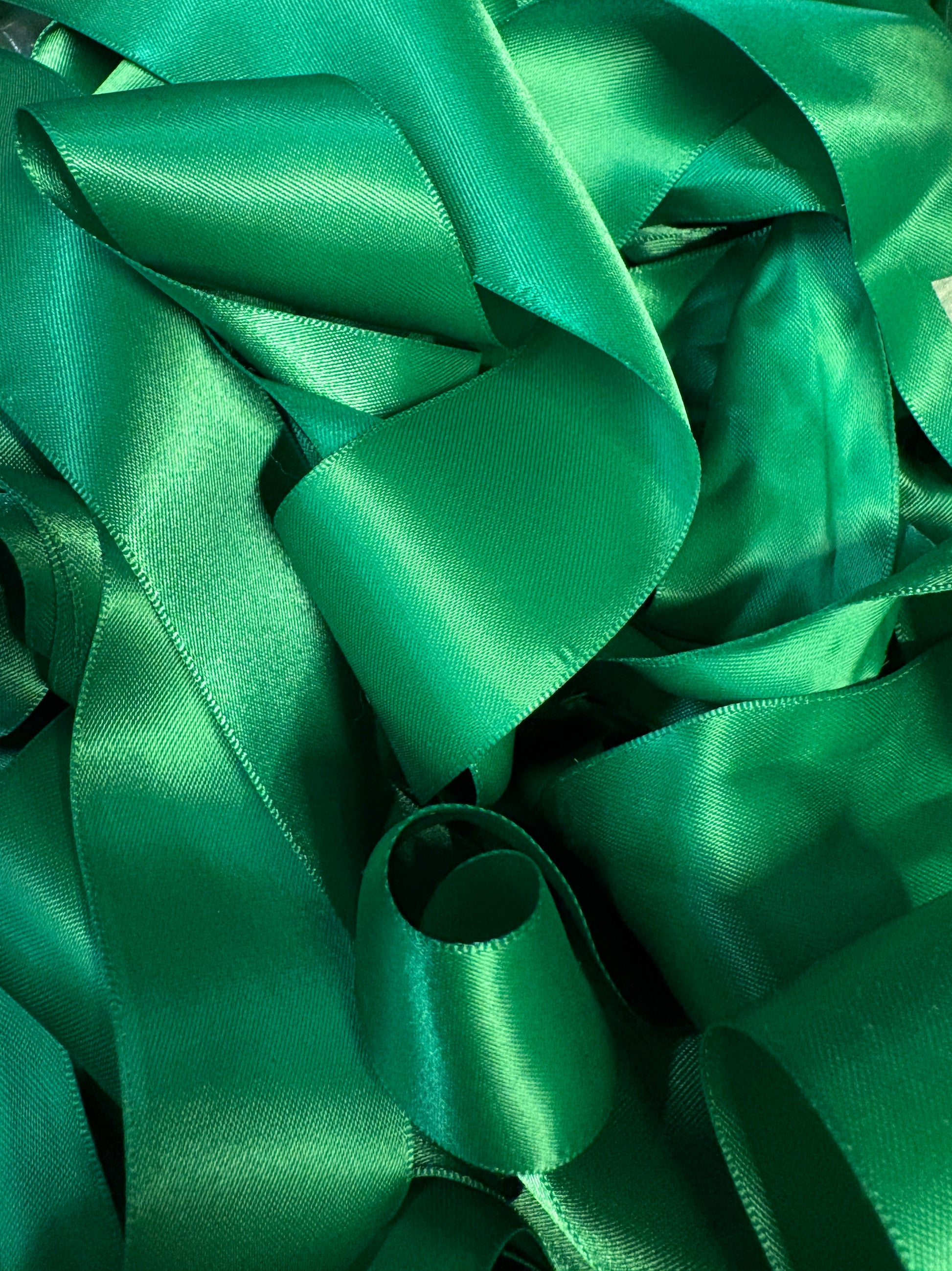 A pile of emerald green satin ribbons layered in soft folds.