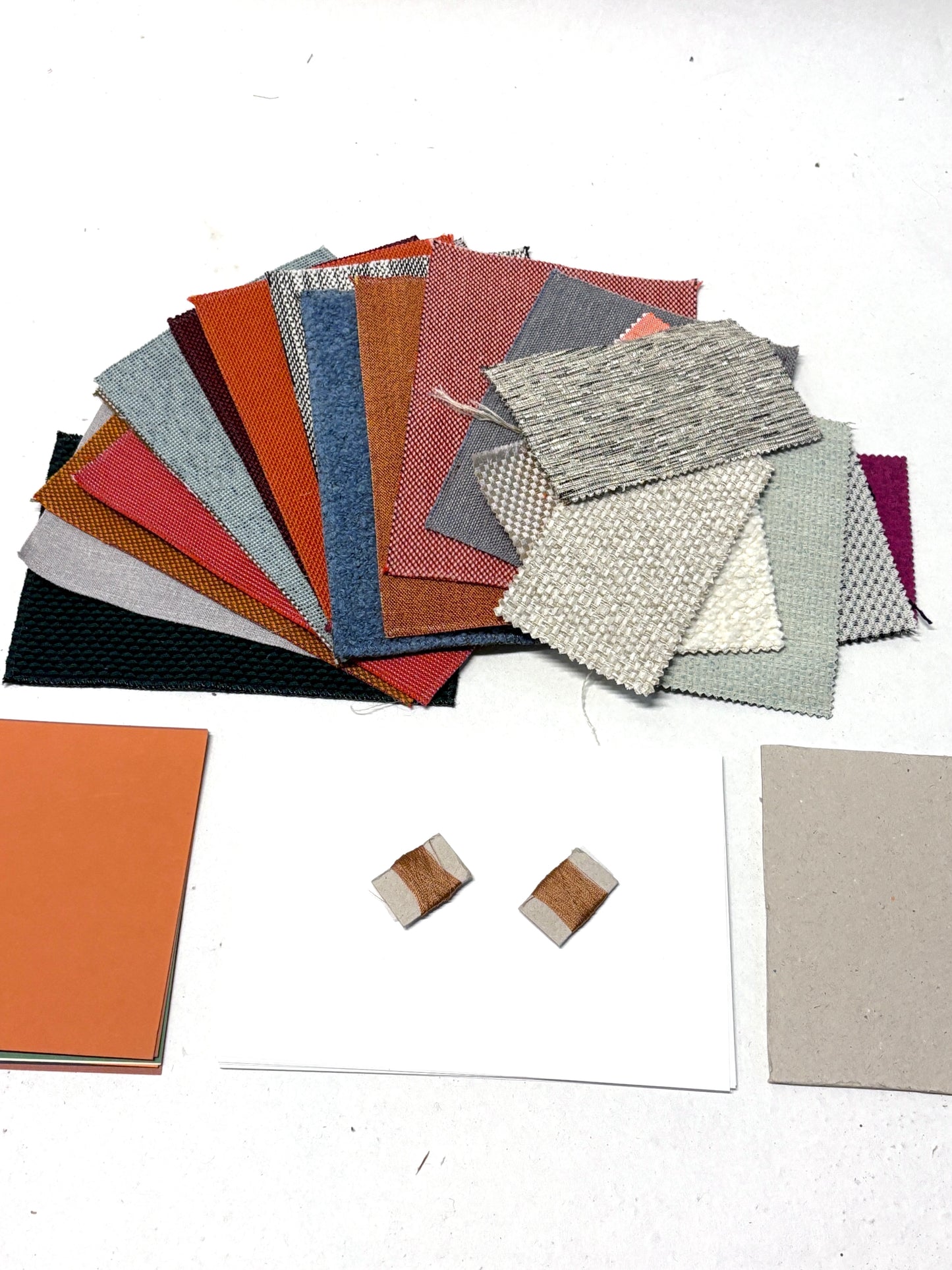Assorted fabric swatches, sample cards and thread details arranged on a white surface.