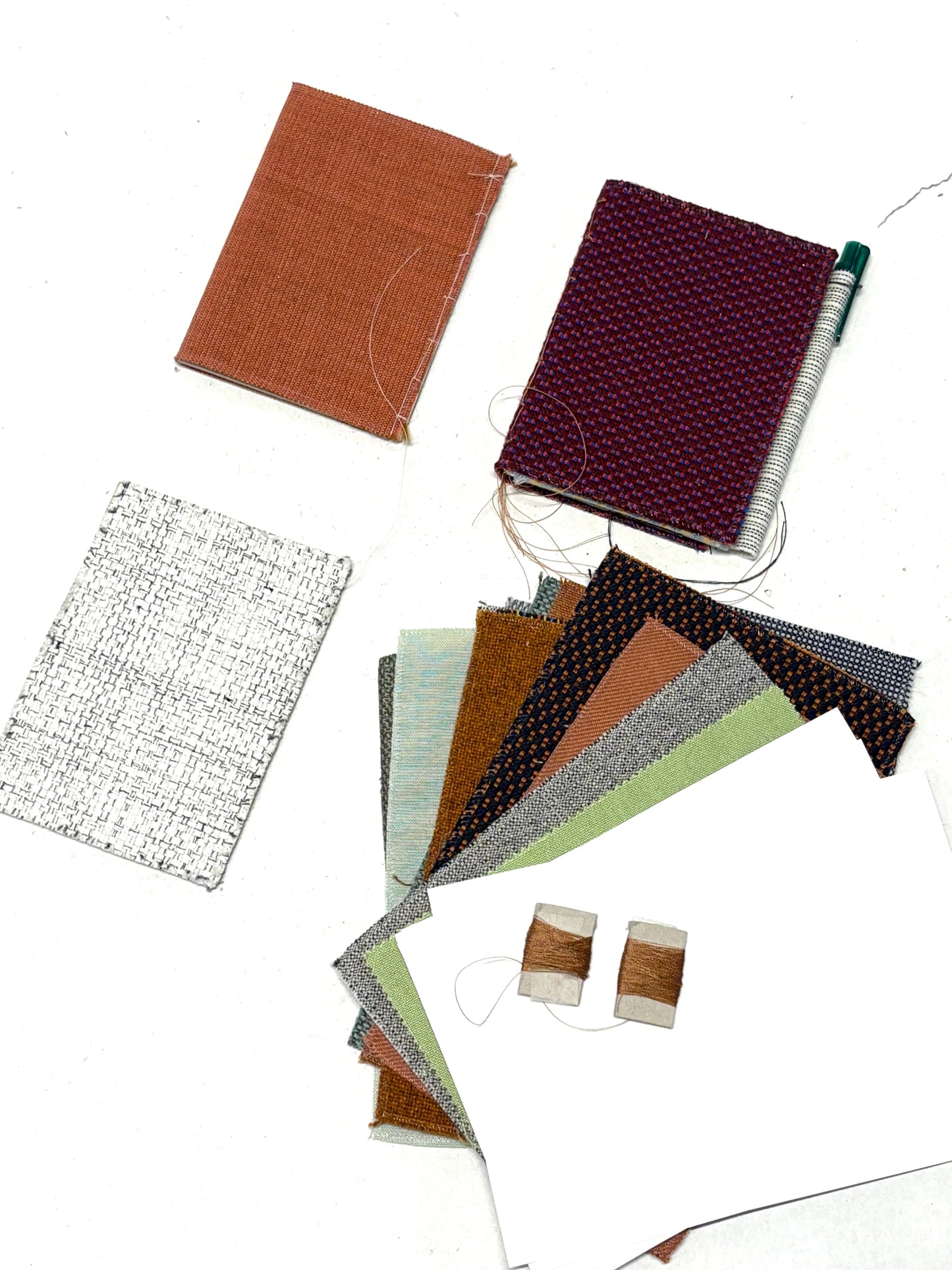 Flat lay of handmade notebook samples with fabric swatches, thread and paper.