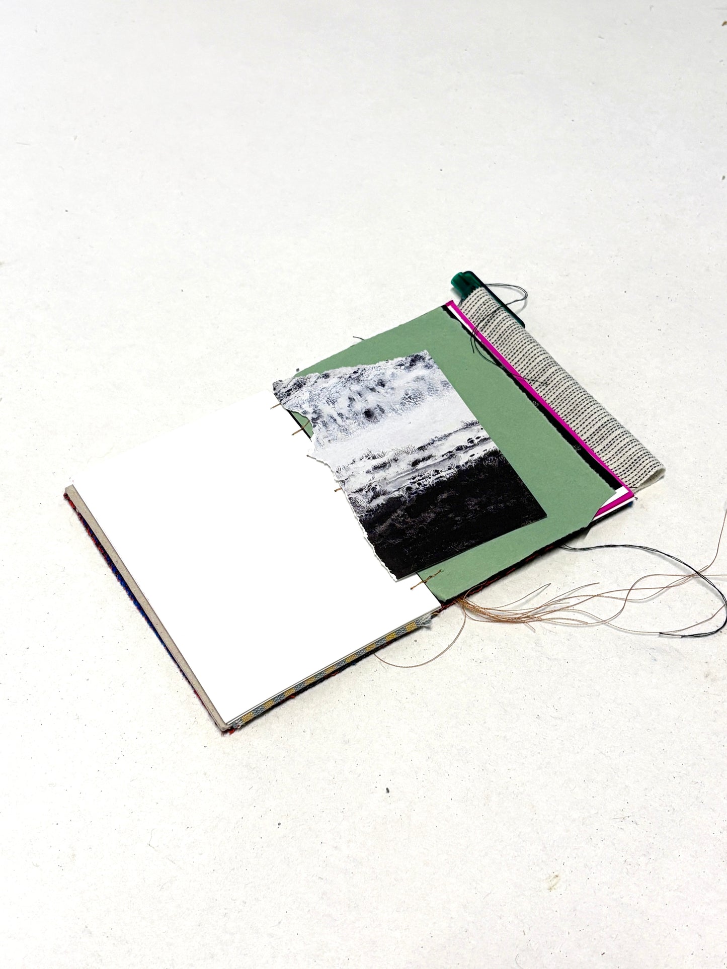 An in-progress fabric-covered notebook displayed with paper inserts and thread.