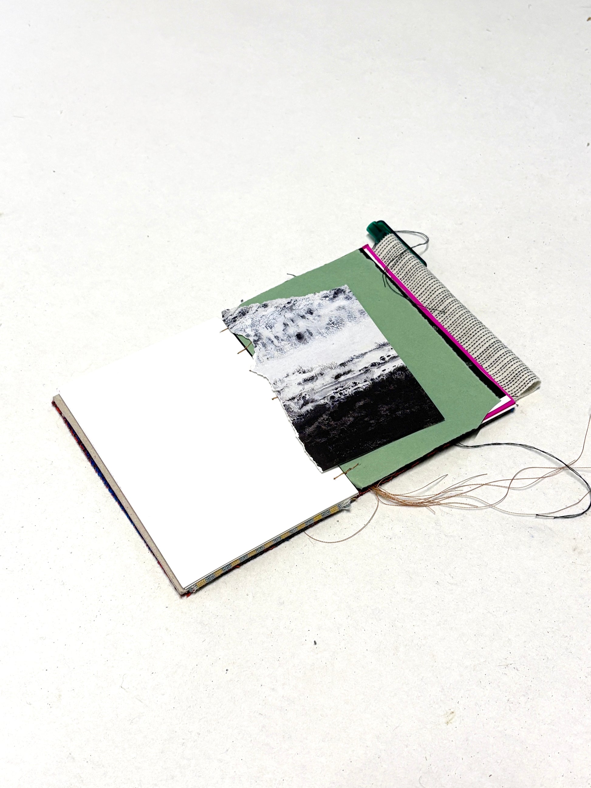 An in-progress fabric-covered notebook displayed with paper inserts and thread.