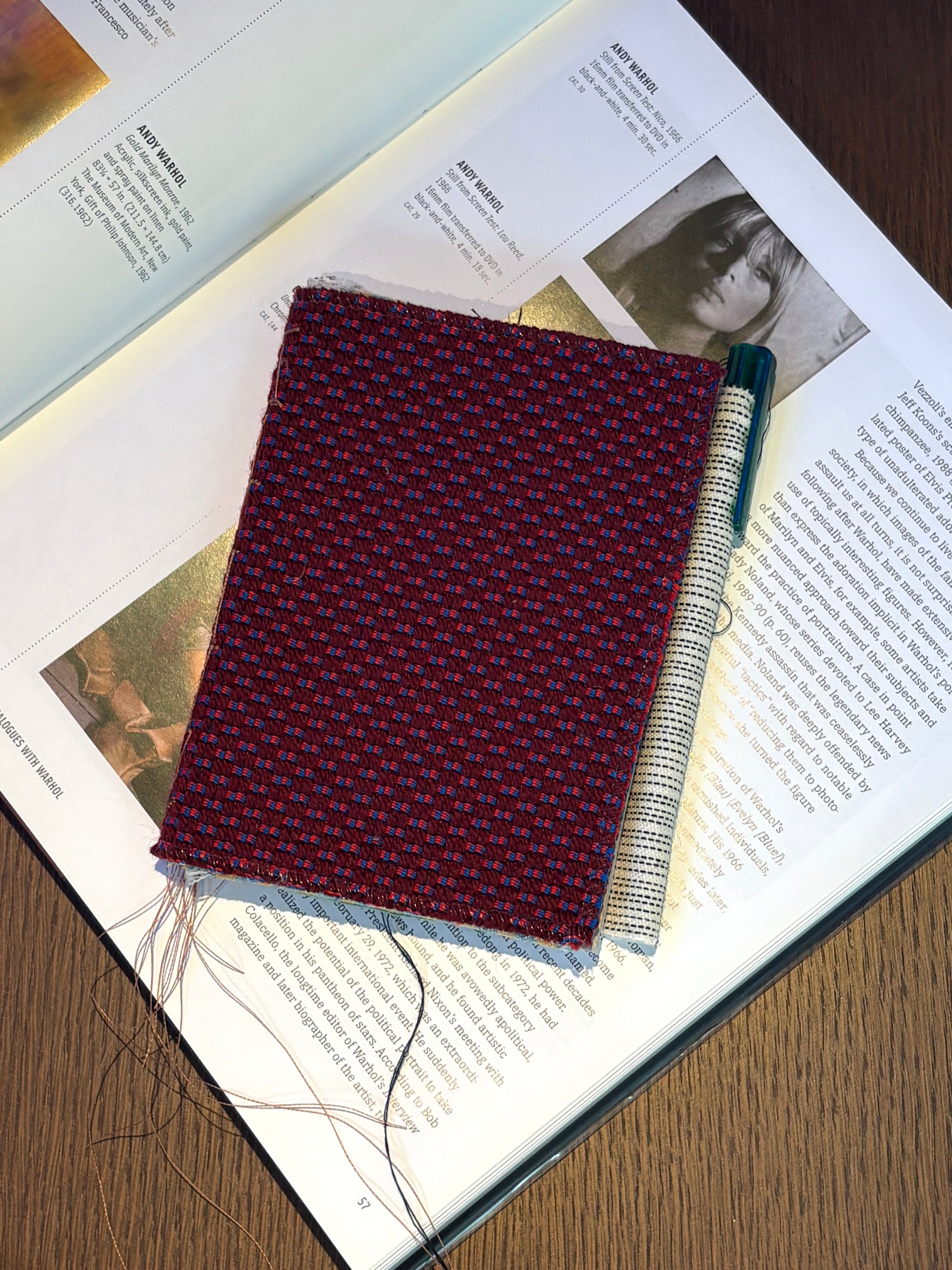 Handmade fabric-covered notebook placed on an open art book with a pen.
