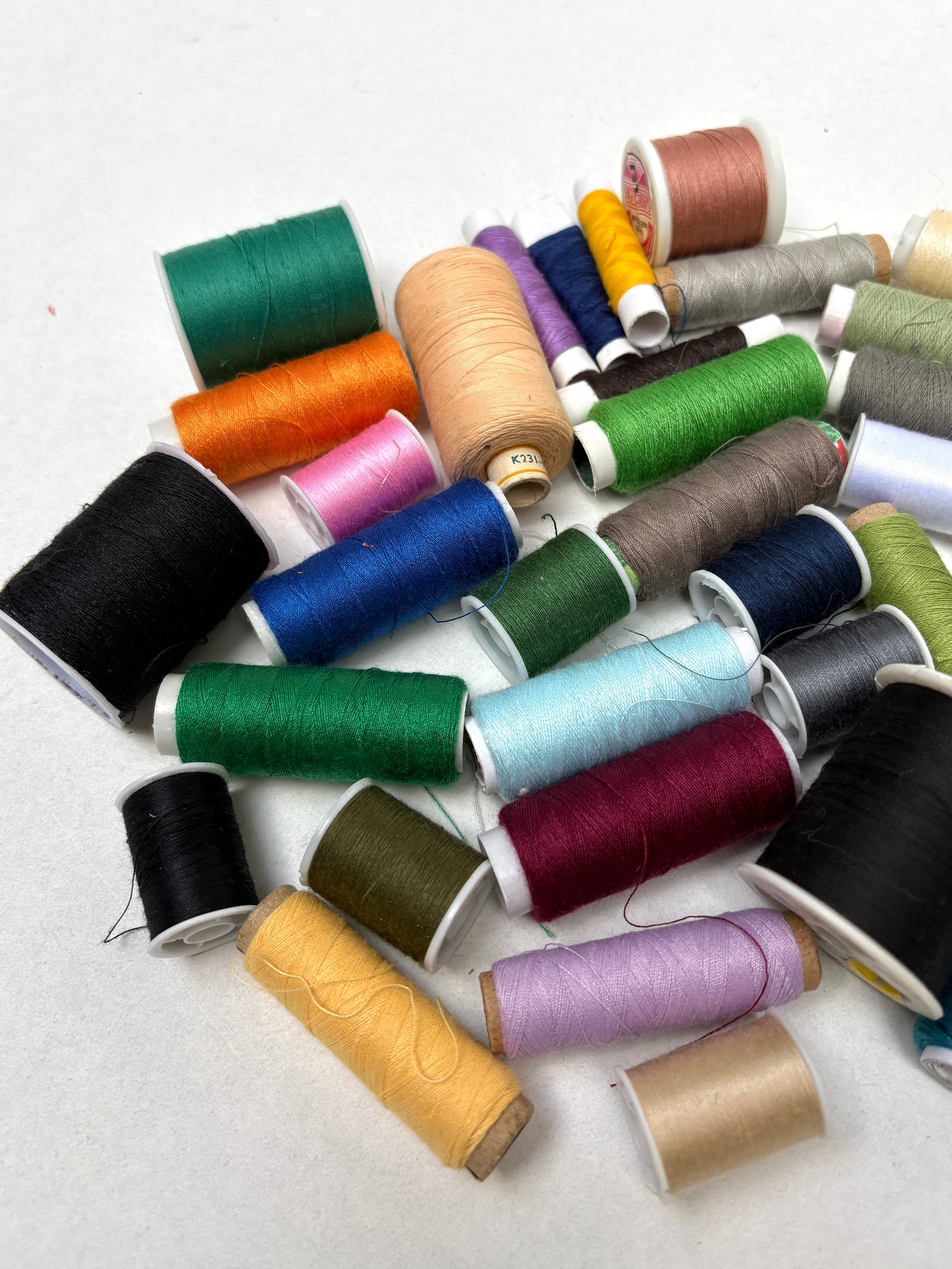 Assorted sewing thread spools in mixed colours scattered on a white background.