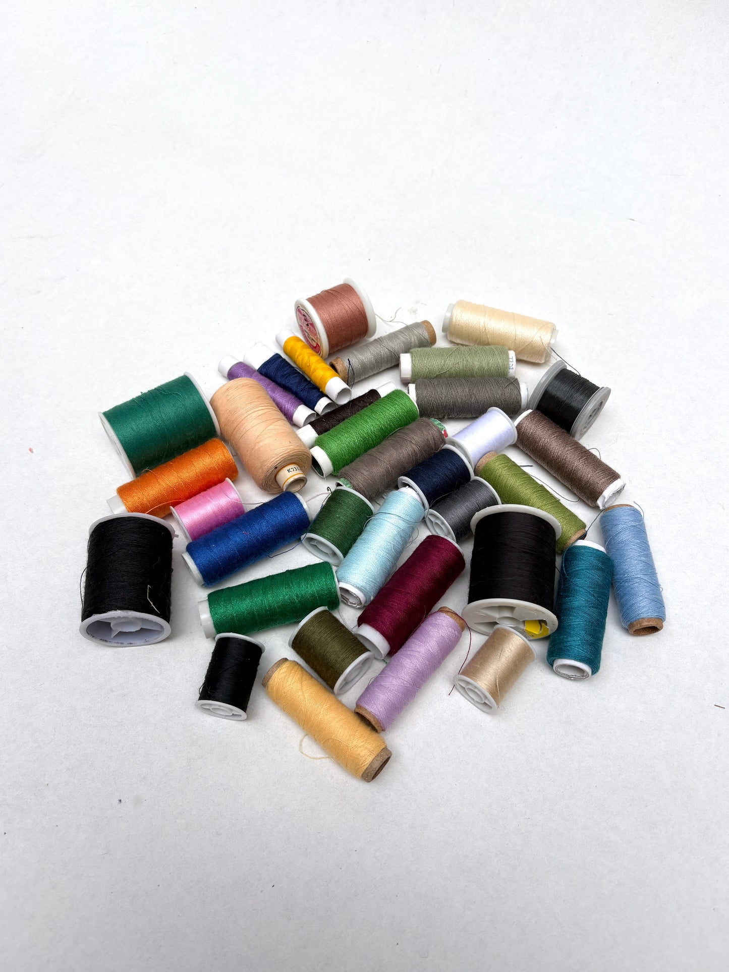 Assorted sewing thread spools in mixed colours arranged on a white background.