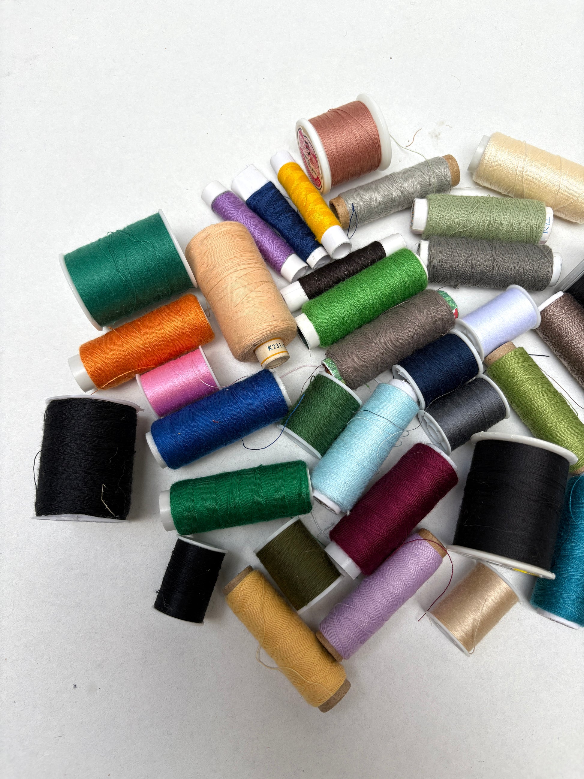 Mixed sewing thread spools in assorted colours displayed on a white background.