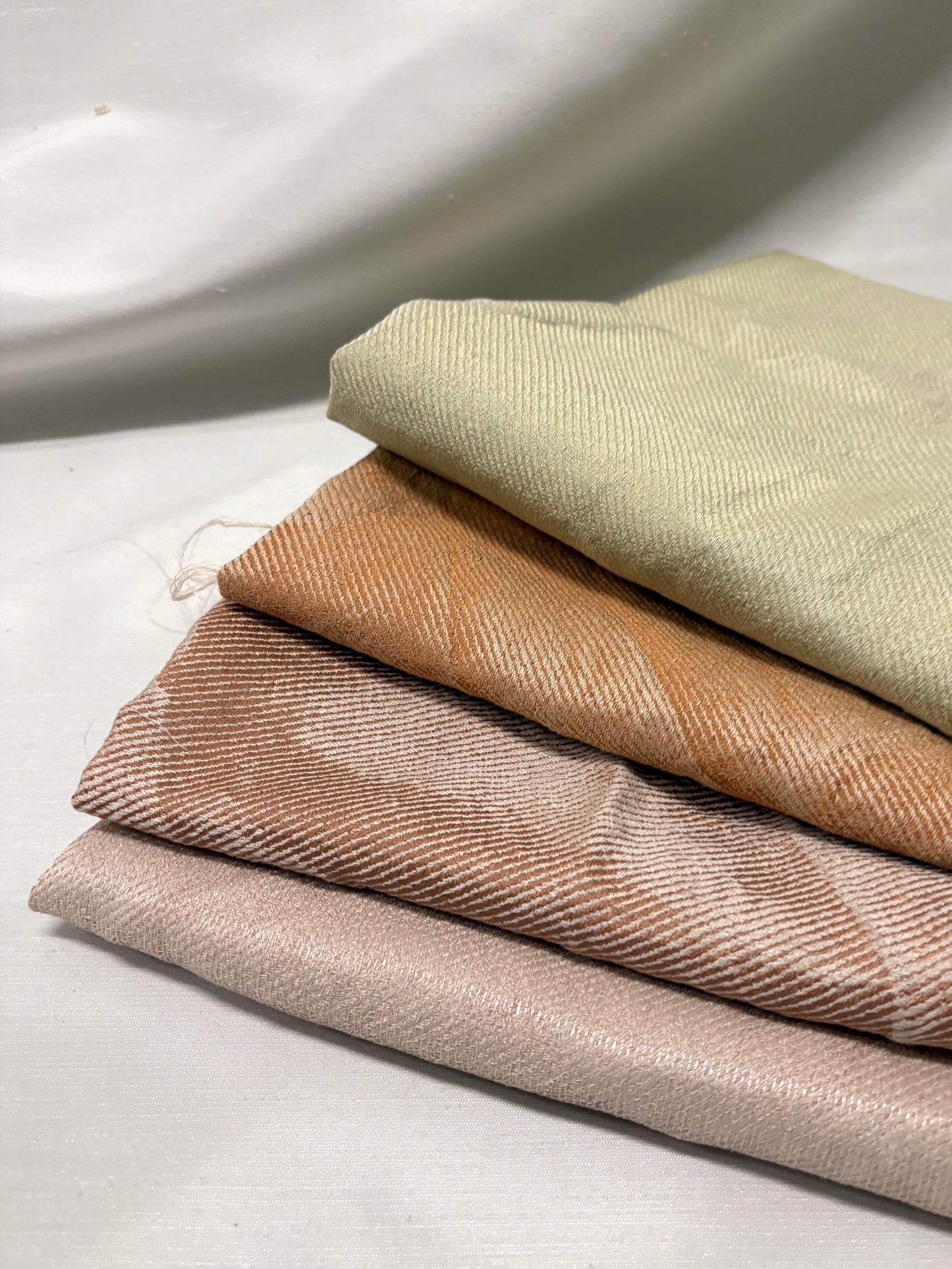 Stack of fabric swatches in beige, brown, and green on a light background