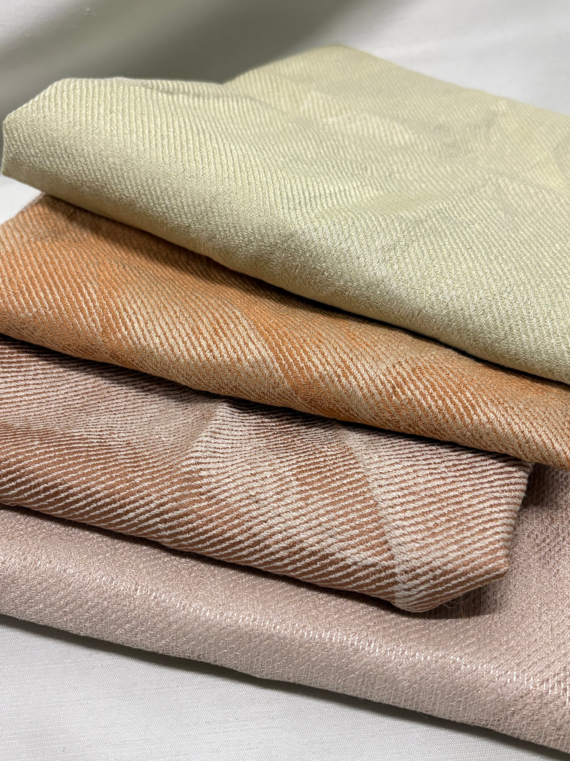 Close-up of stacked fabric swatches in beige, brown and green tones.