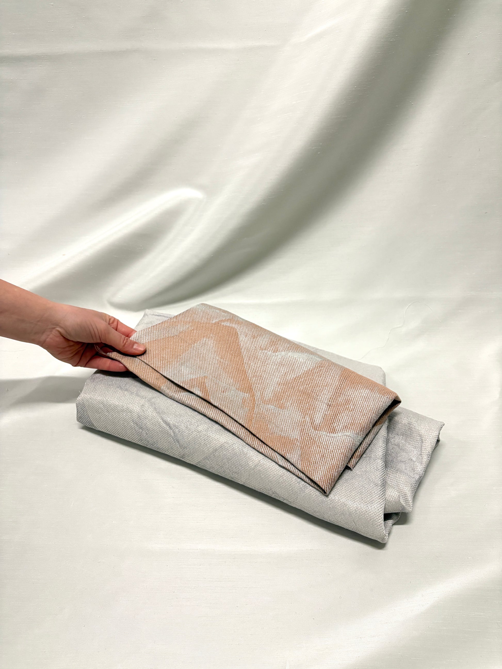 Hand holding folded neutral fabrics with subtle woven texture and pattern.