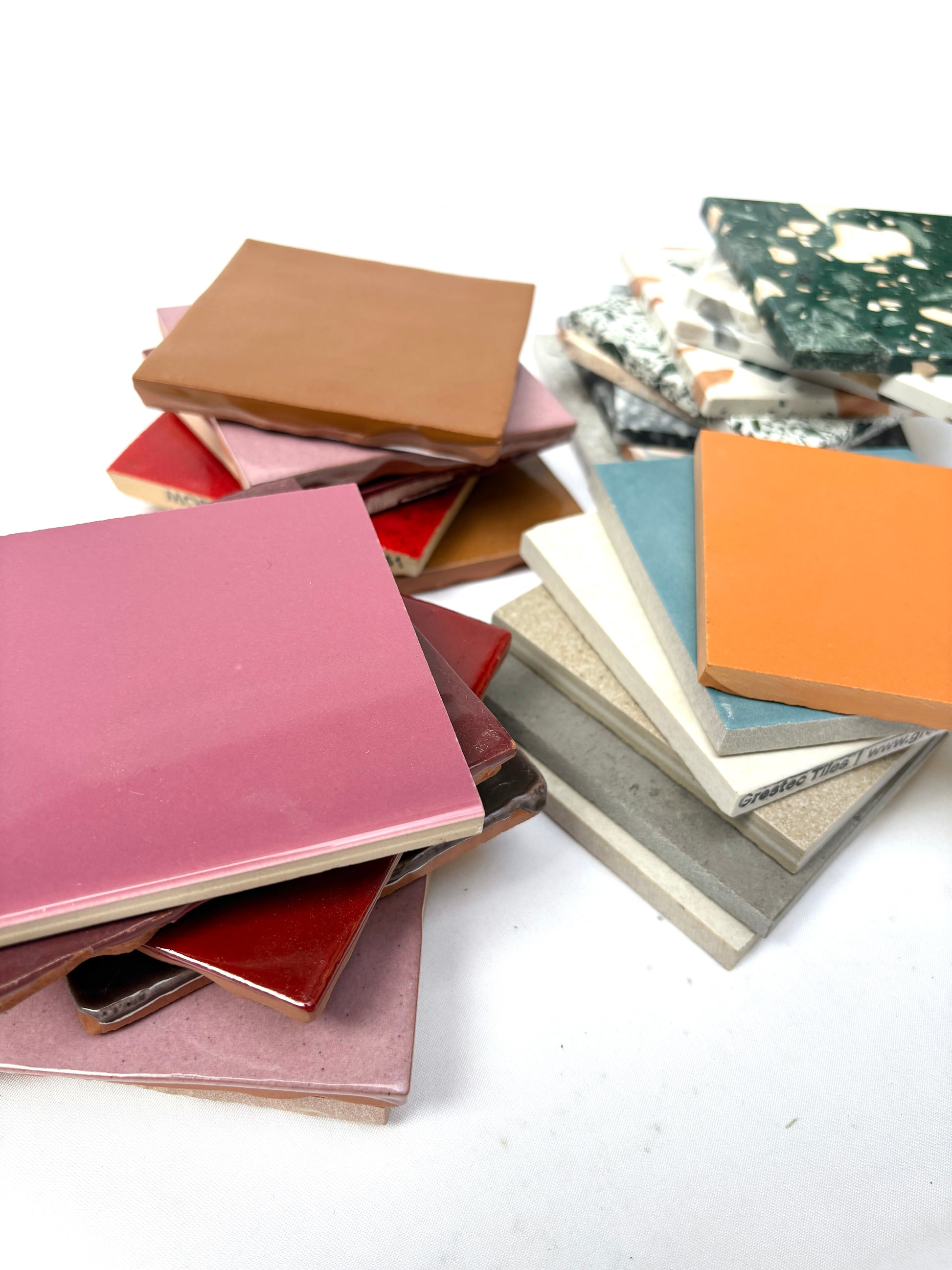 Coloured sample tiles are stacked in a loose pile on white