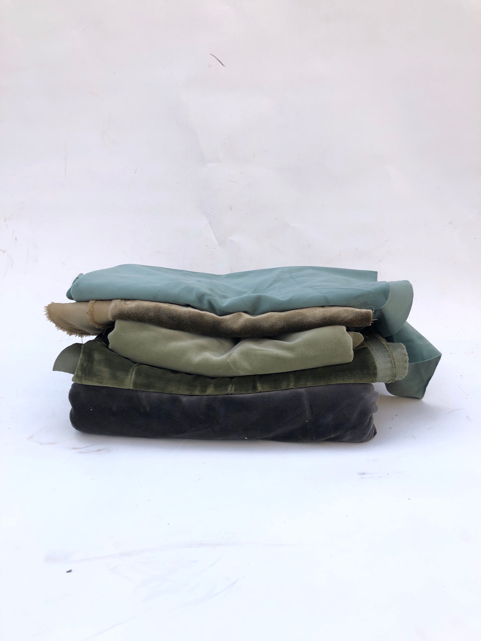 Velvet fabric pieces are stacked in a soft folded pile on white