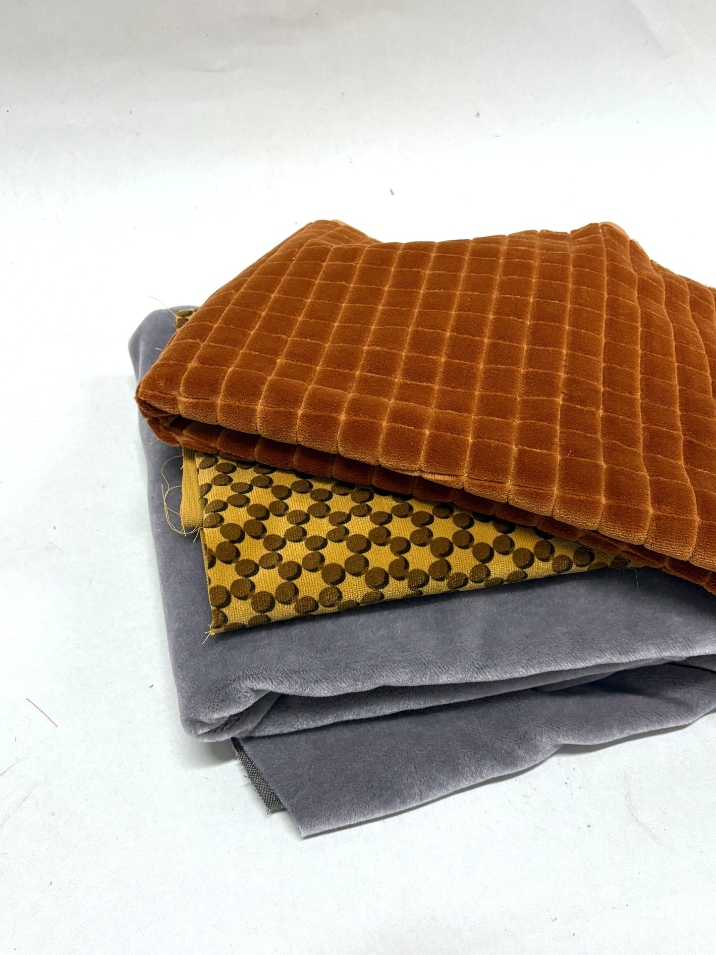 Folded fabric pieces in mixed colours are layered on a white surface