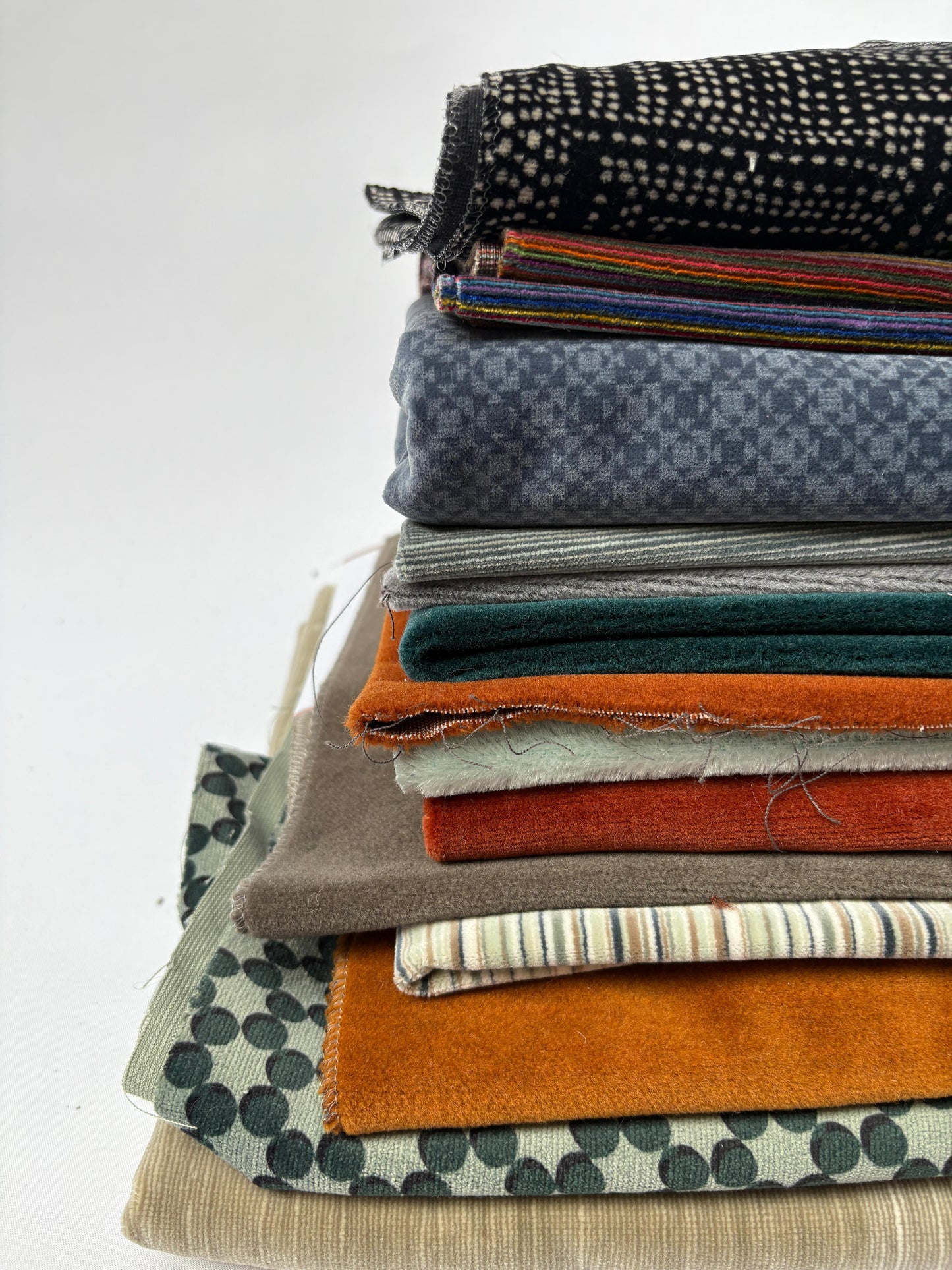 Stacked mixed fabric pieces in assorted colours, textures and patterns on white.