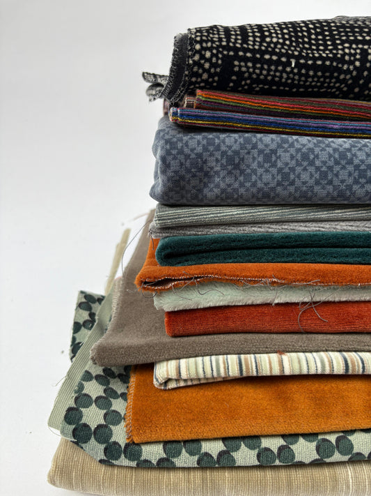 Stacked mixed fabric pieces in assorted colours, textures and patterns on white.