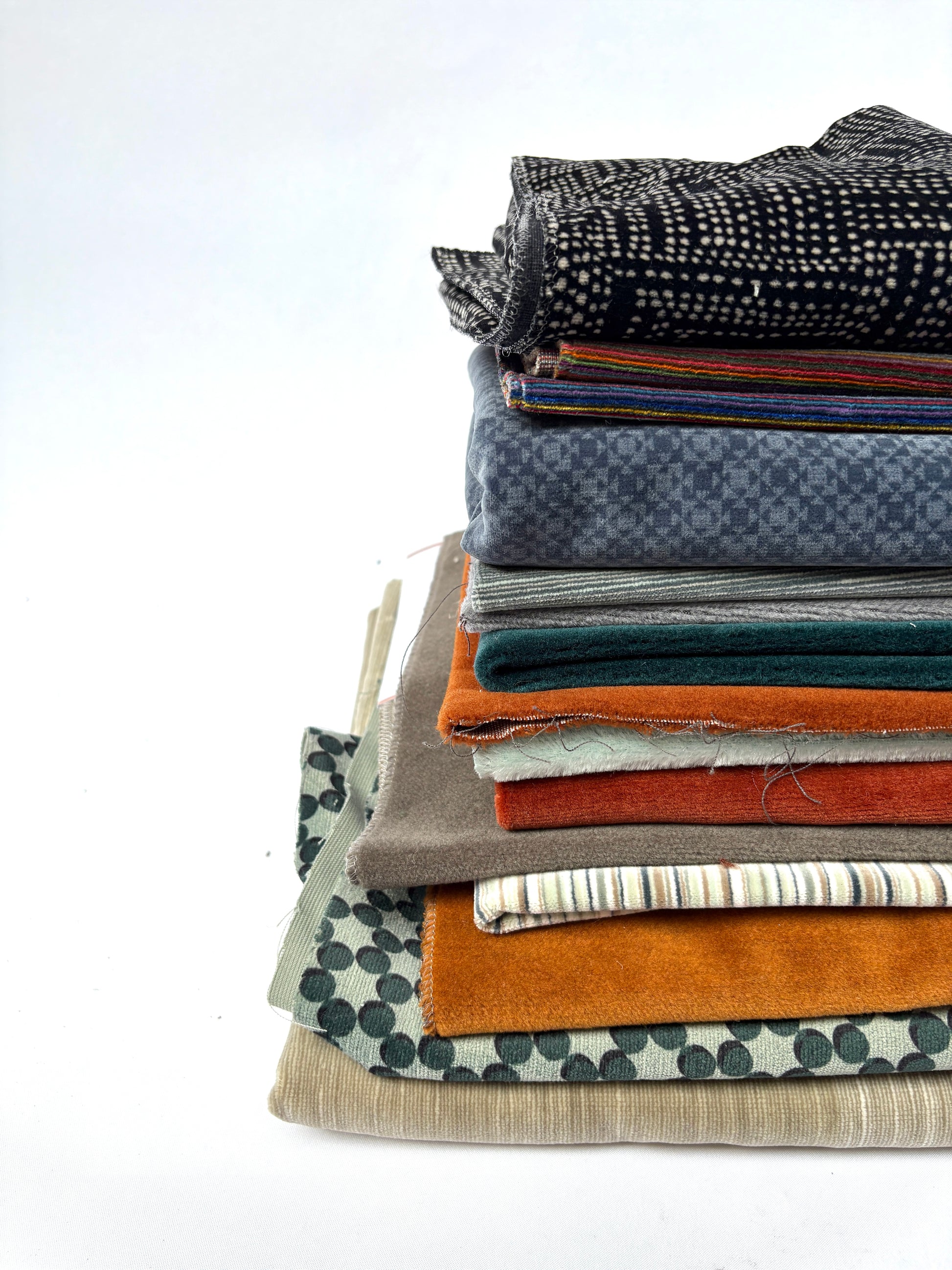 Stacked mixed fabric pieces in assorted colours, textures and patterns on white.