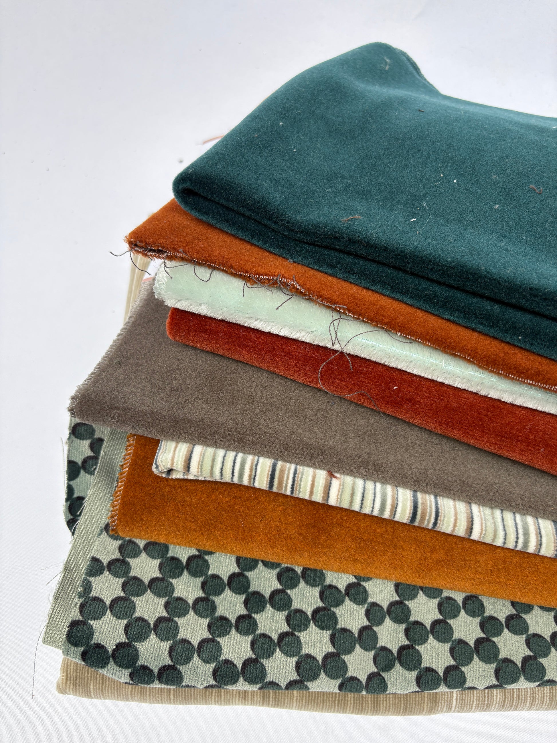 Layered mixed fabric pieces in varied colours, textures and patterns on a white background.