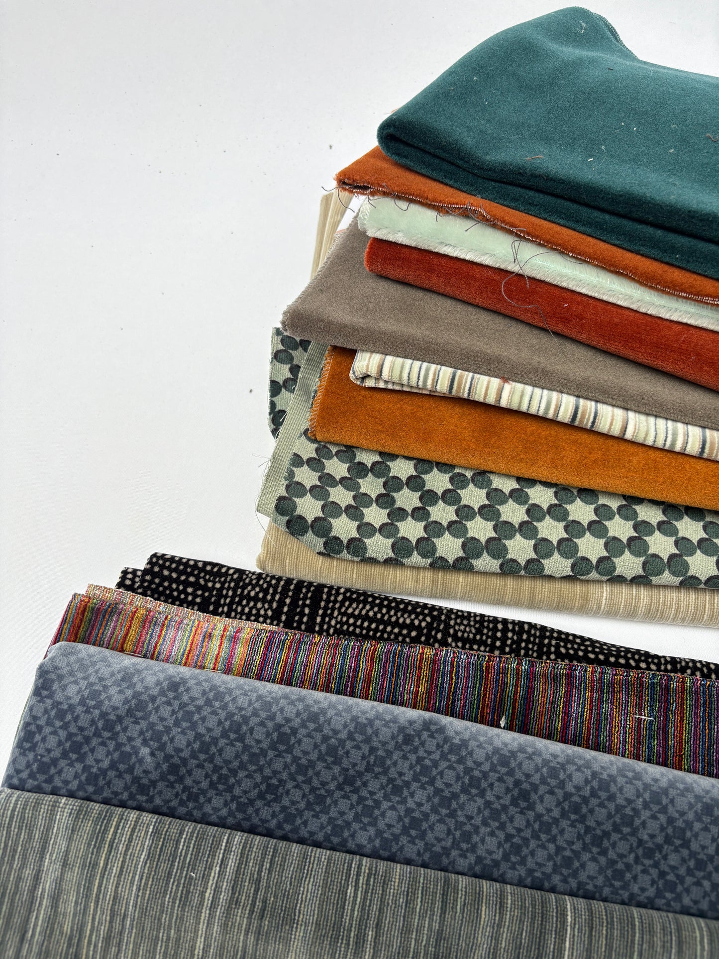 Assorted layered fabric pieces in mixed colours, textures and patterns on white.