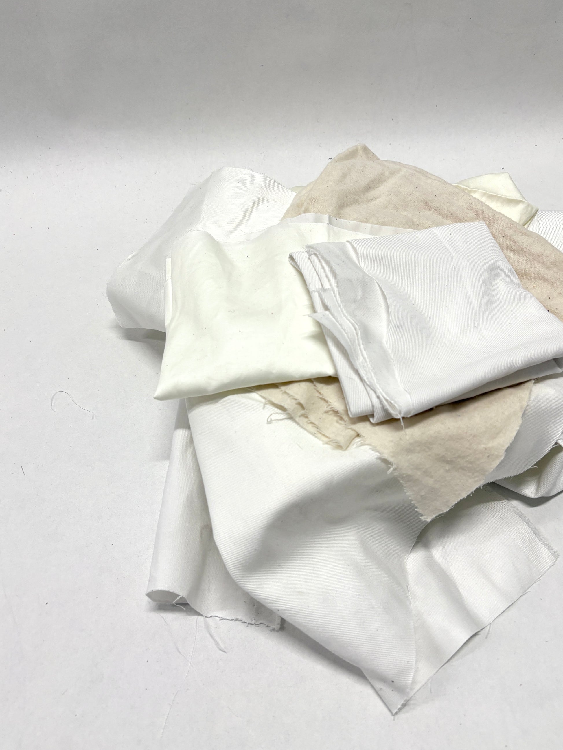 White fabric pieces are stacked in a loose pile on white