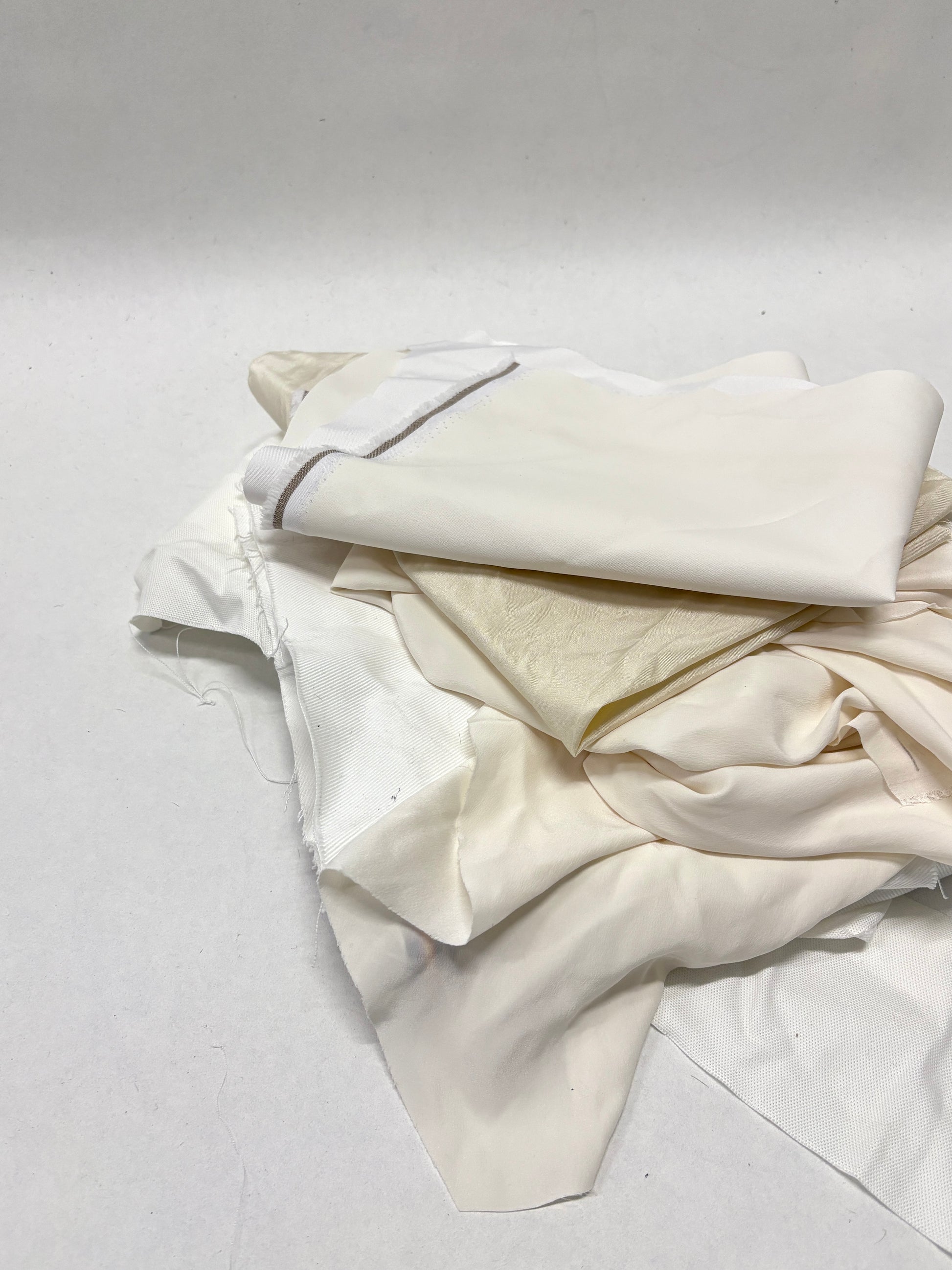 Folded white fabric offcuts are arranged on a white surface