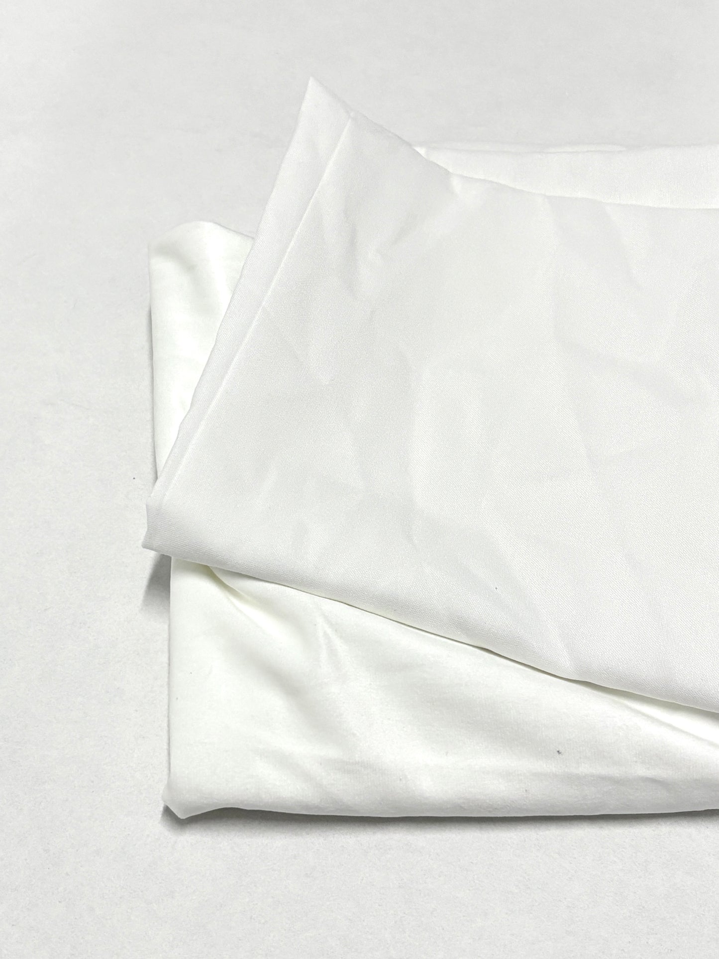 Folded white fabric pieces are stacked neatly on a white surface