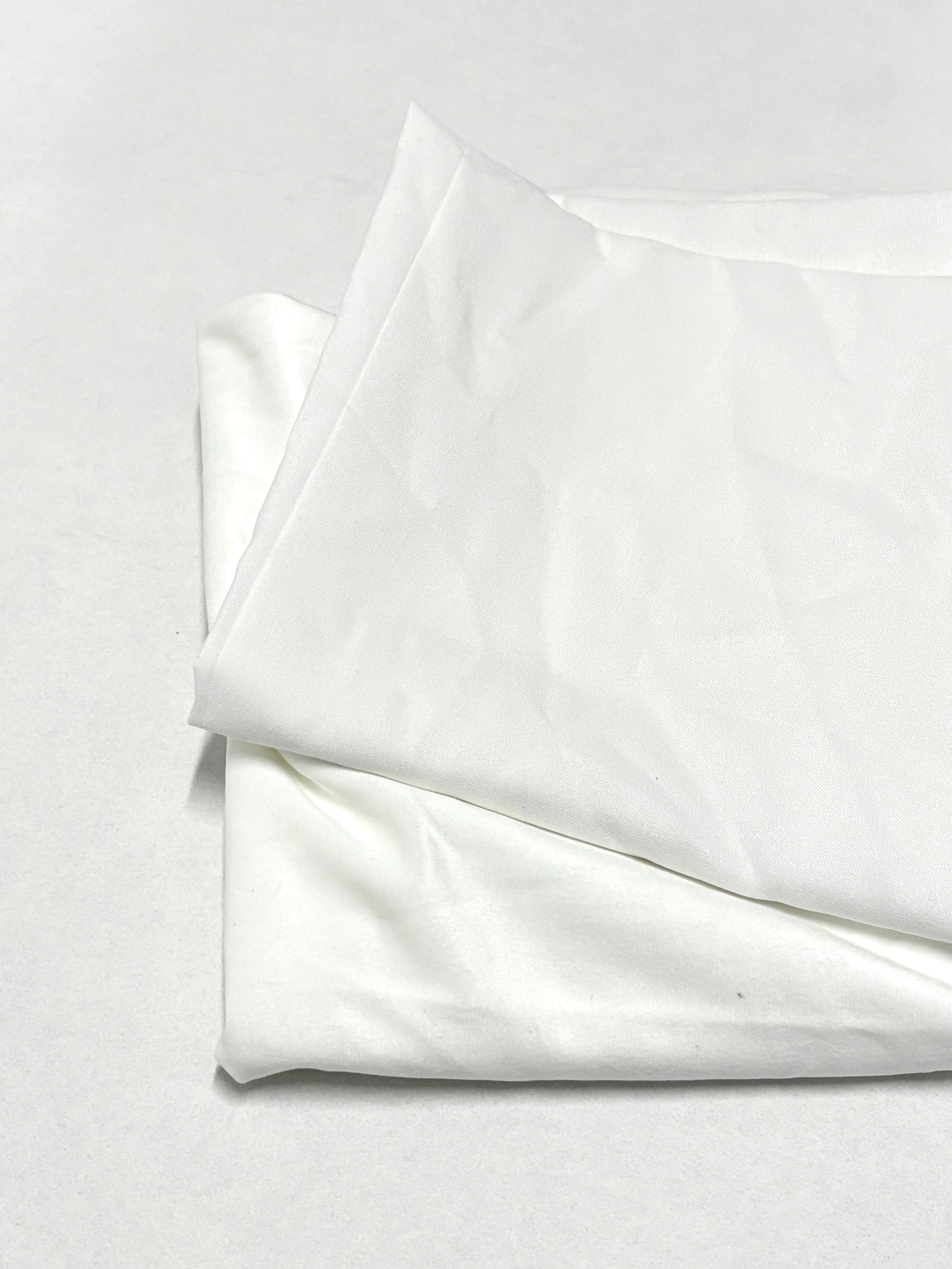 Folded white fabric pieces are stacked neatly on a white surface