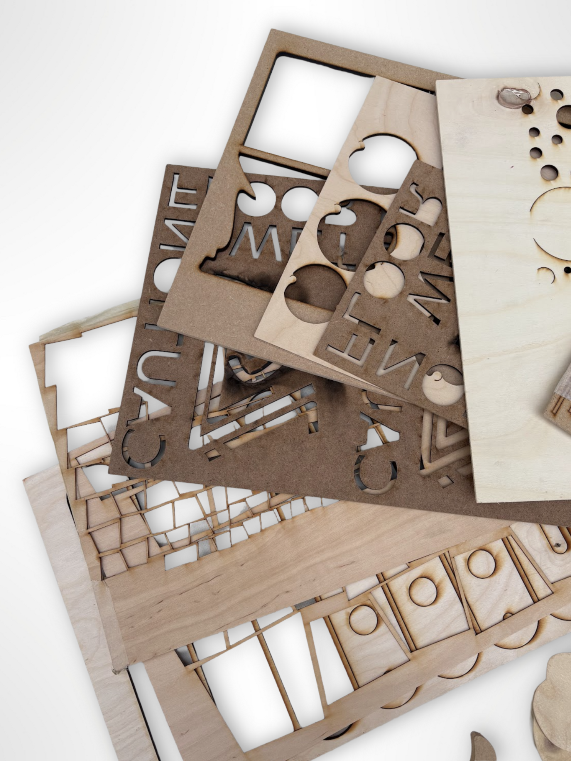 Mixed wooden cut-outs and sample boards are shown in layered piles.