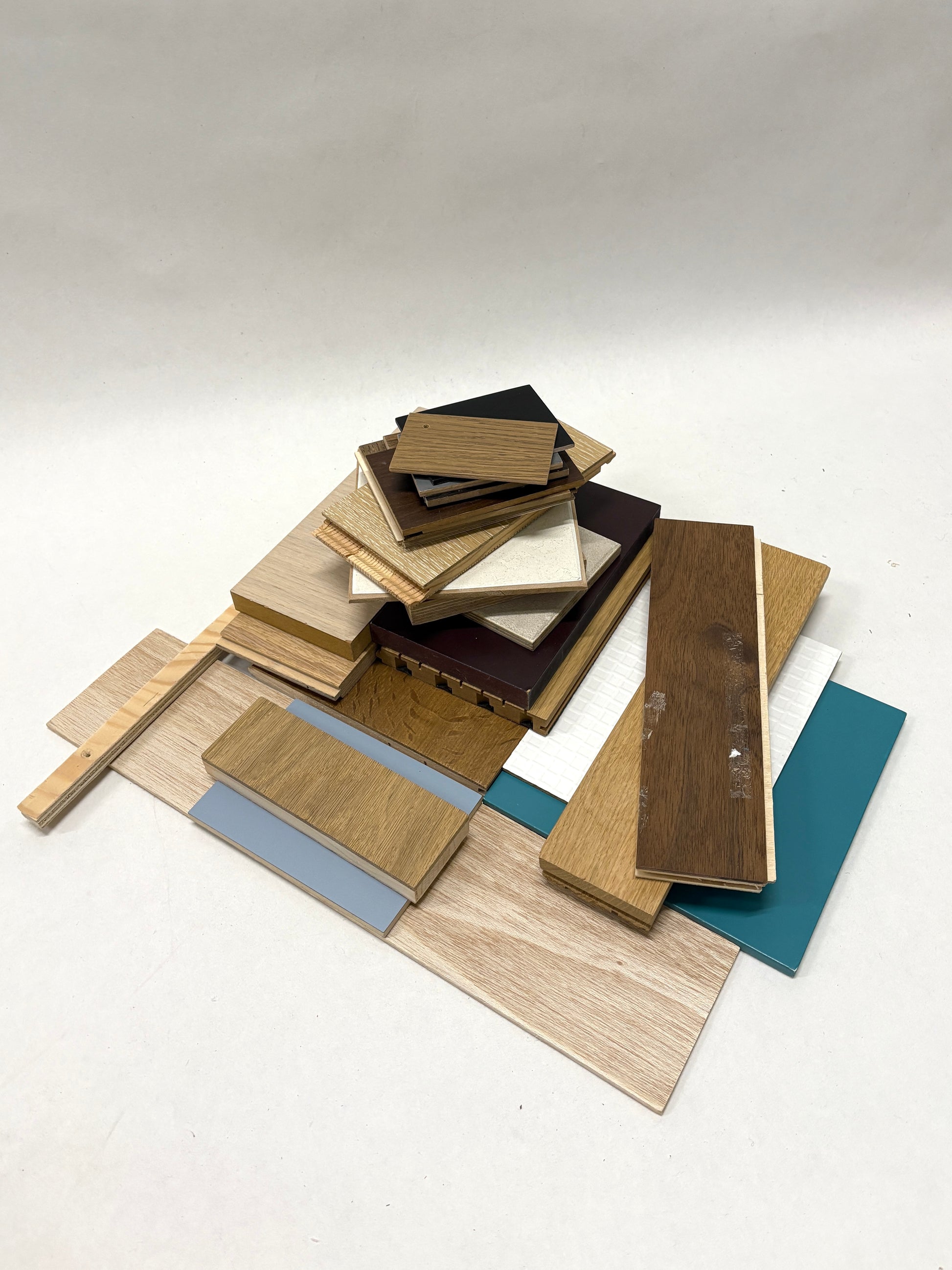Mixed wood sample boards are stacked in a layered pile on white