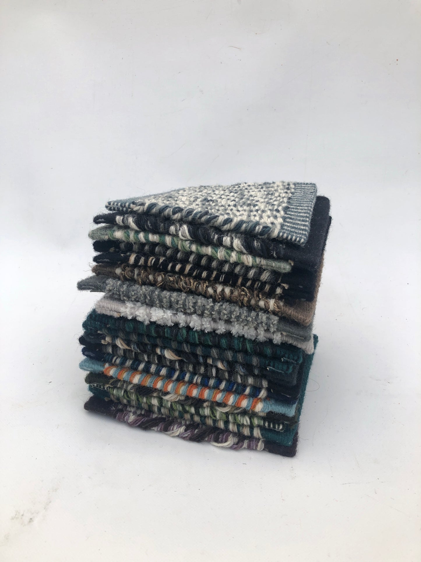 Textured fabric swatches are stacked in a neat pile on white