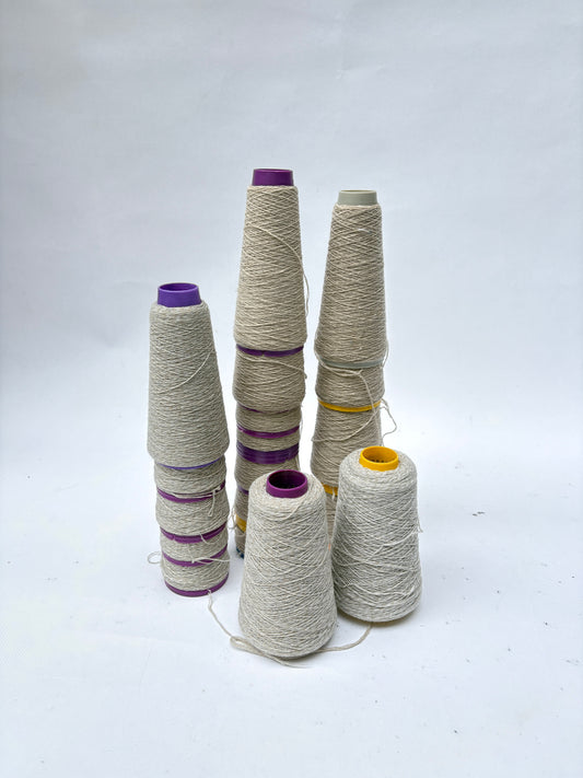Several cones of off-white thread stand on a white surface