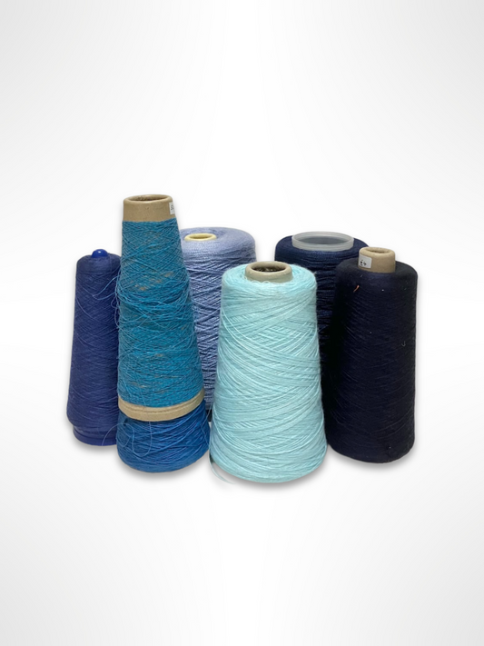 A collection of yarn cones in various shades of blue and pink, arranged in a group against a white background.