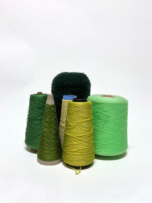 A collection of green yarn cones in various shades, displayed on a white background.