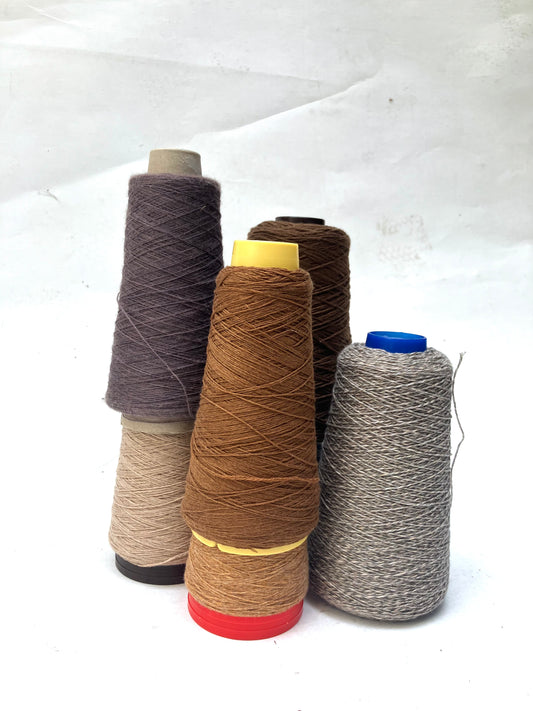 Assorted yarn cones in muted neutral shades displayed on a white background.