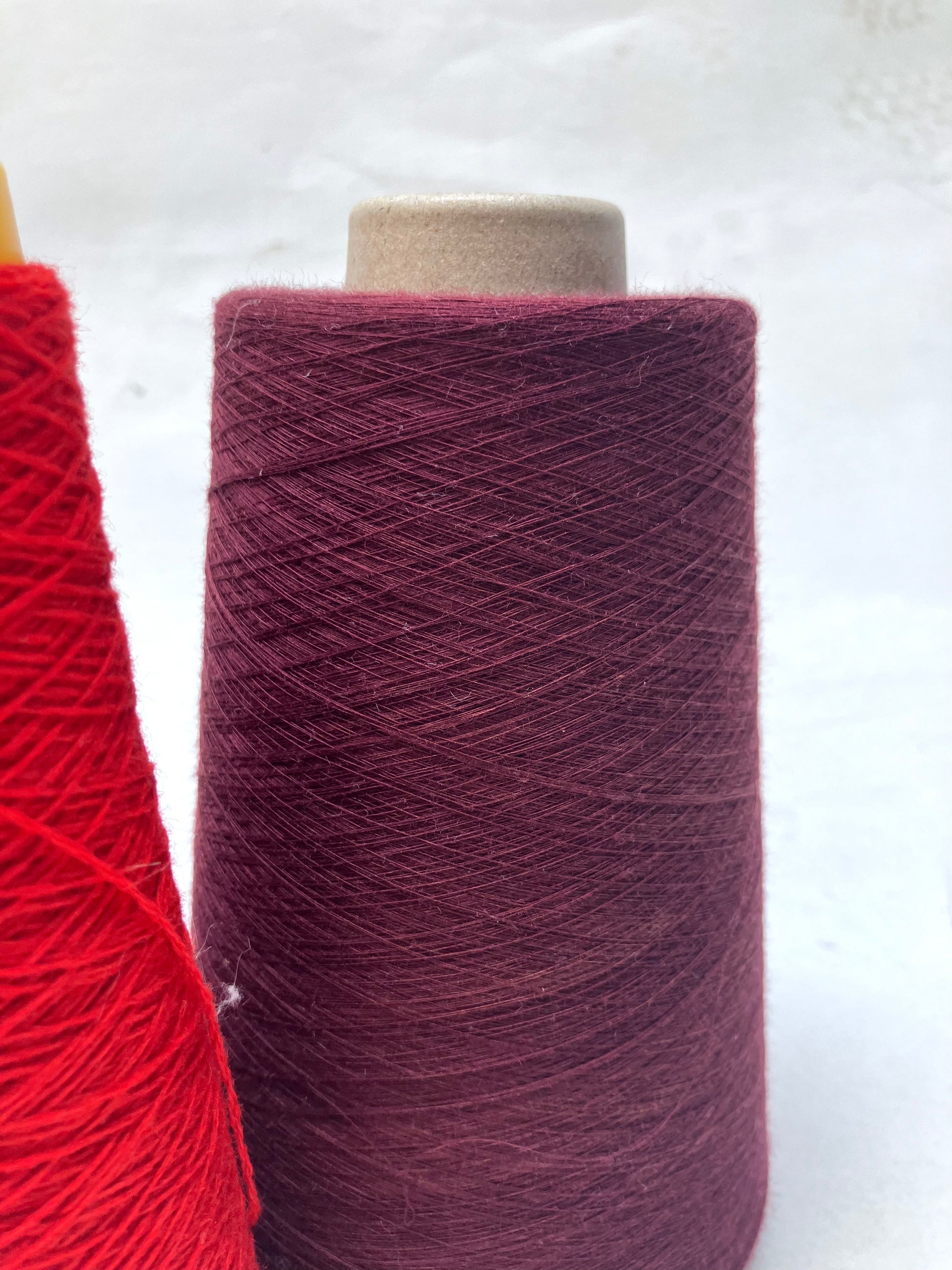 Close-up of yarn cones in bright red and deep burgundy shades on white.
