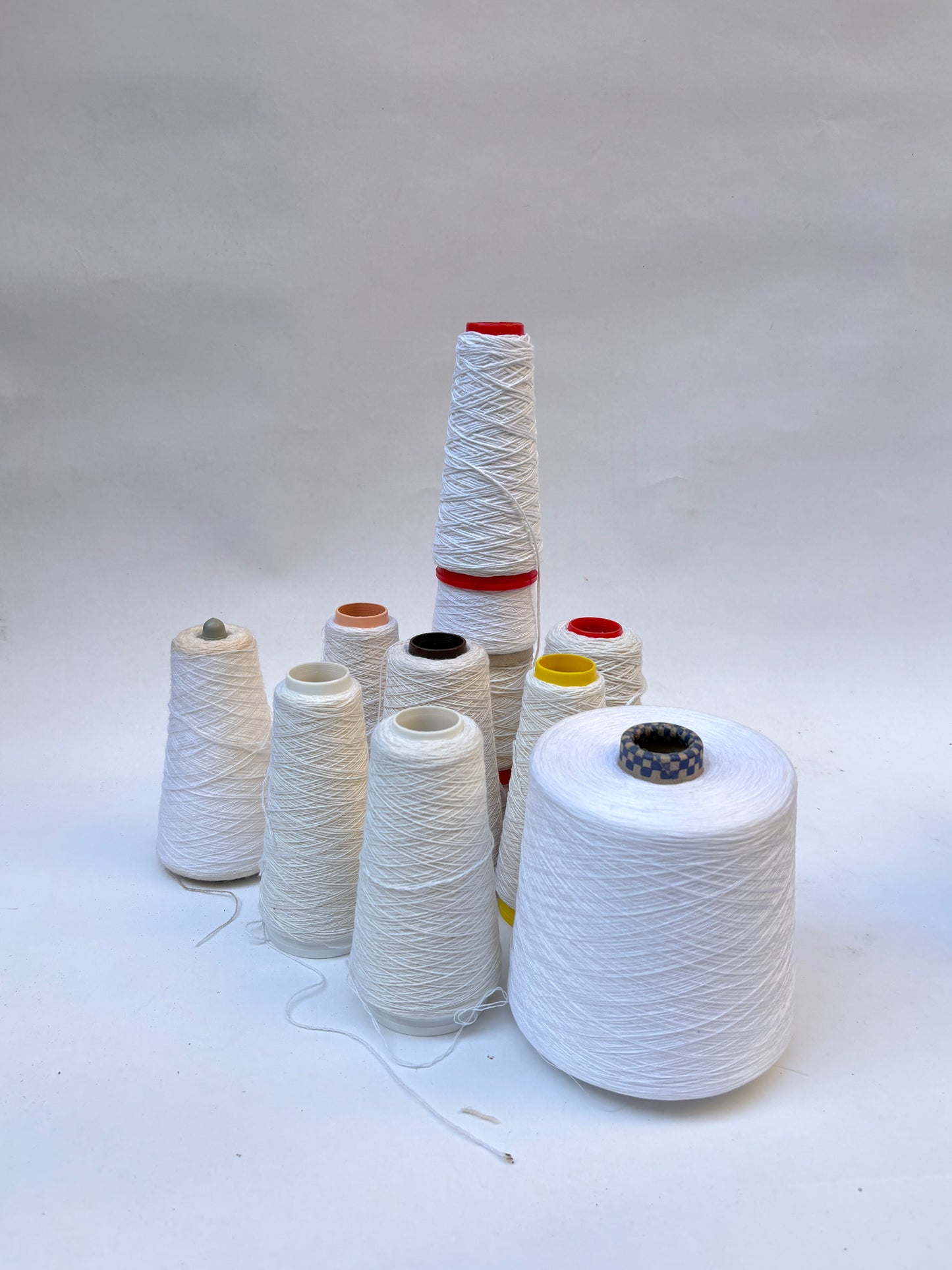 Mixed bundle of yarn cones in white shades displayed on a white background.