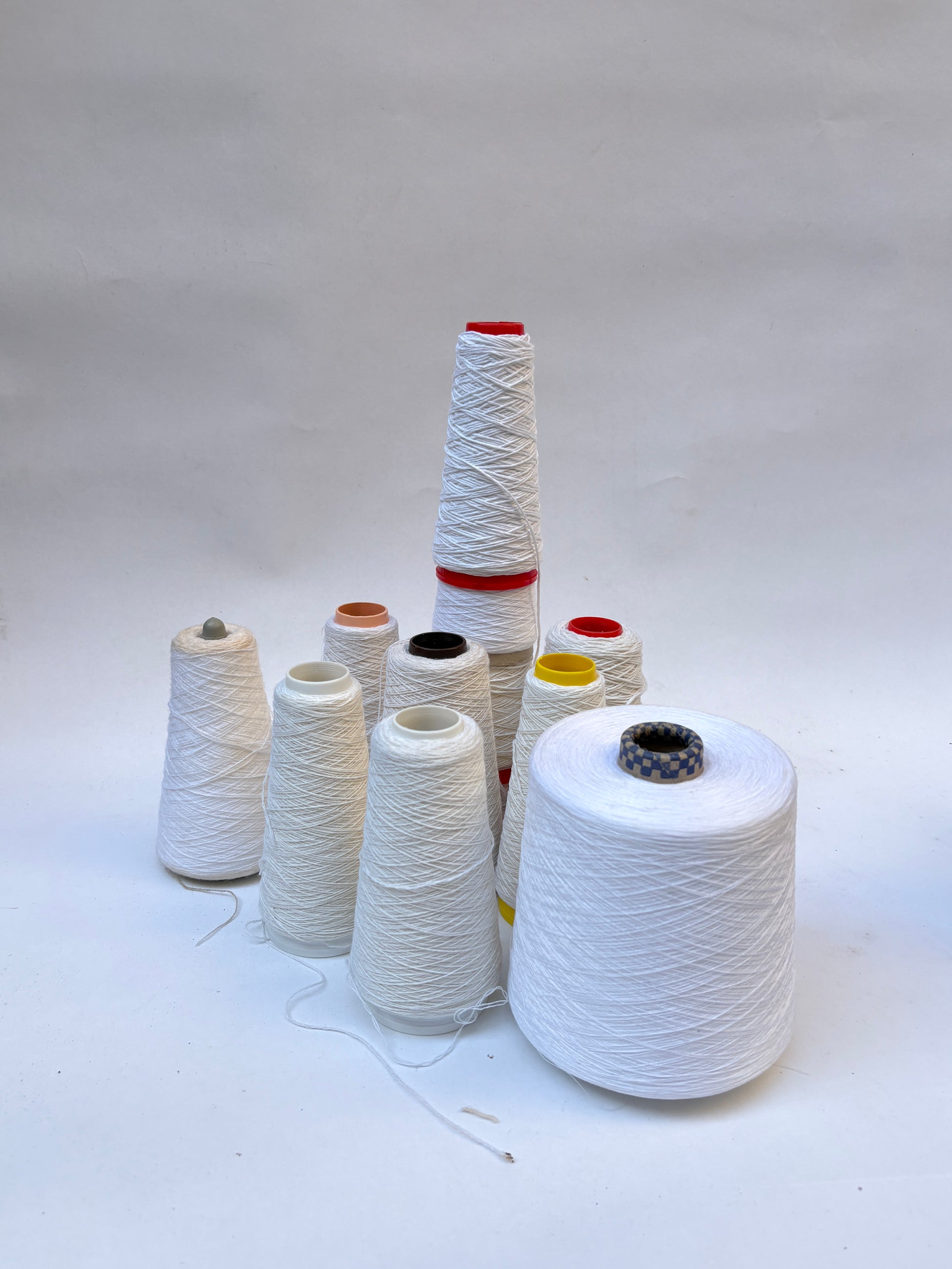 Mixed bundle of yarn cones in white shades displayed on a white background.