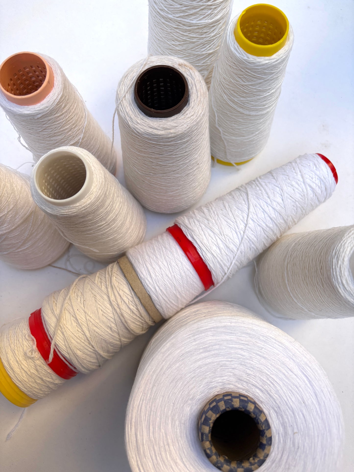 Assorted yarn cones in white shades arranged on a white background.