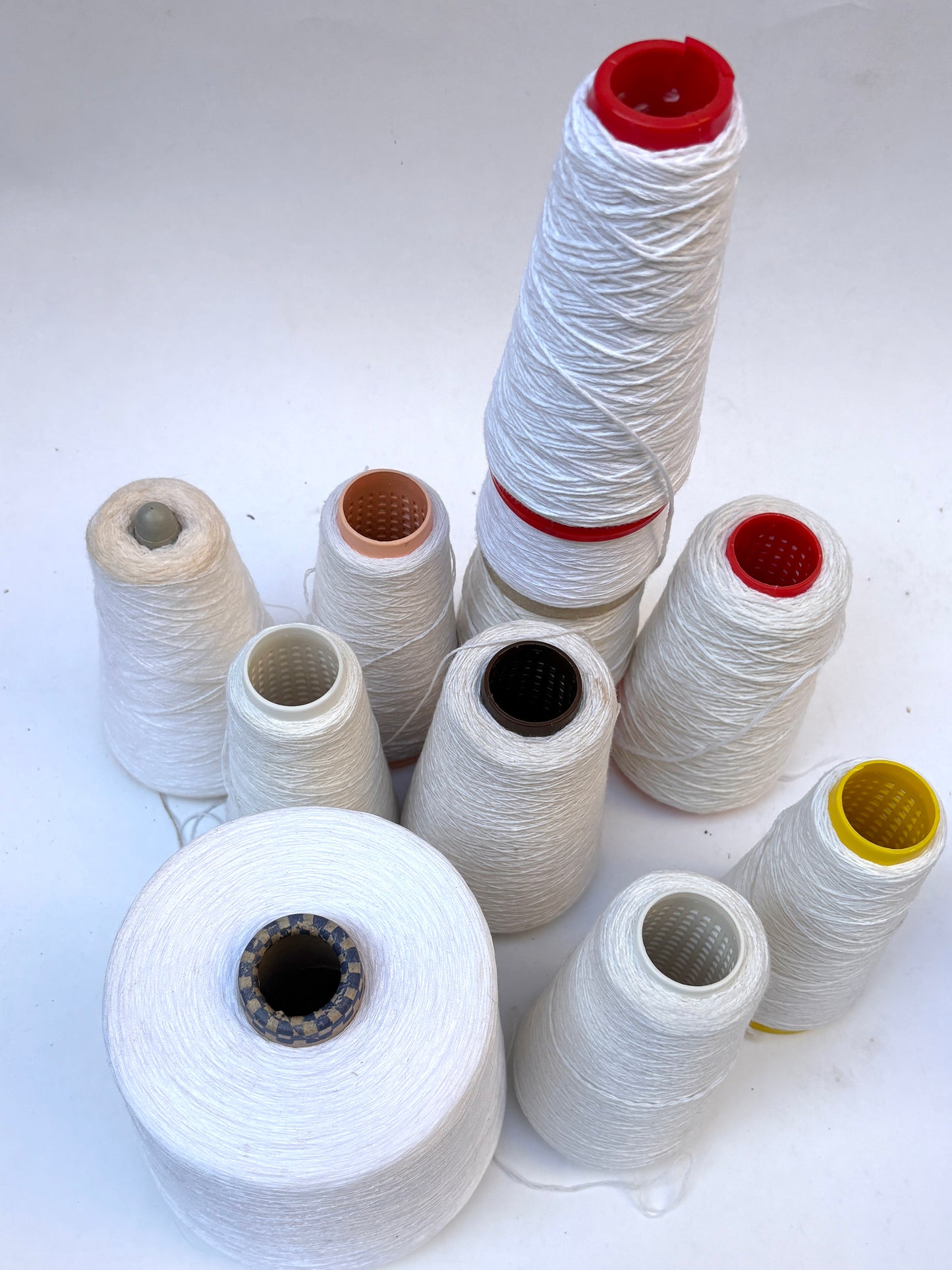 Mixed bundle of white shade yarn cones displayed on a plain white background.