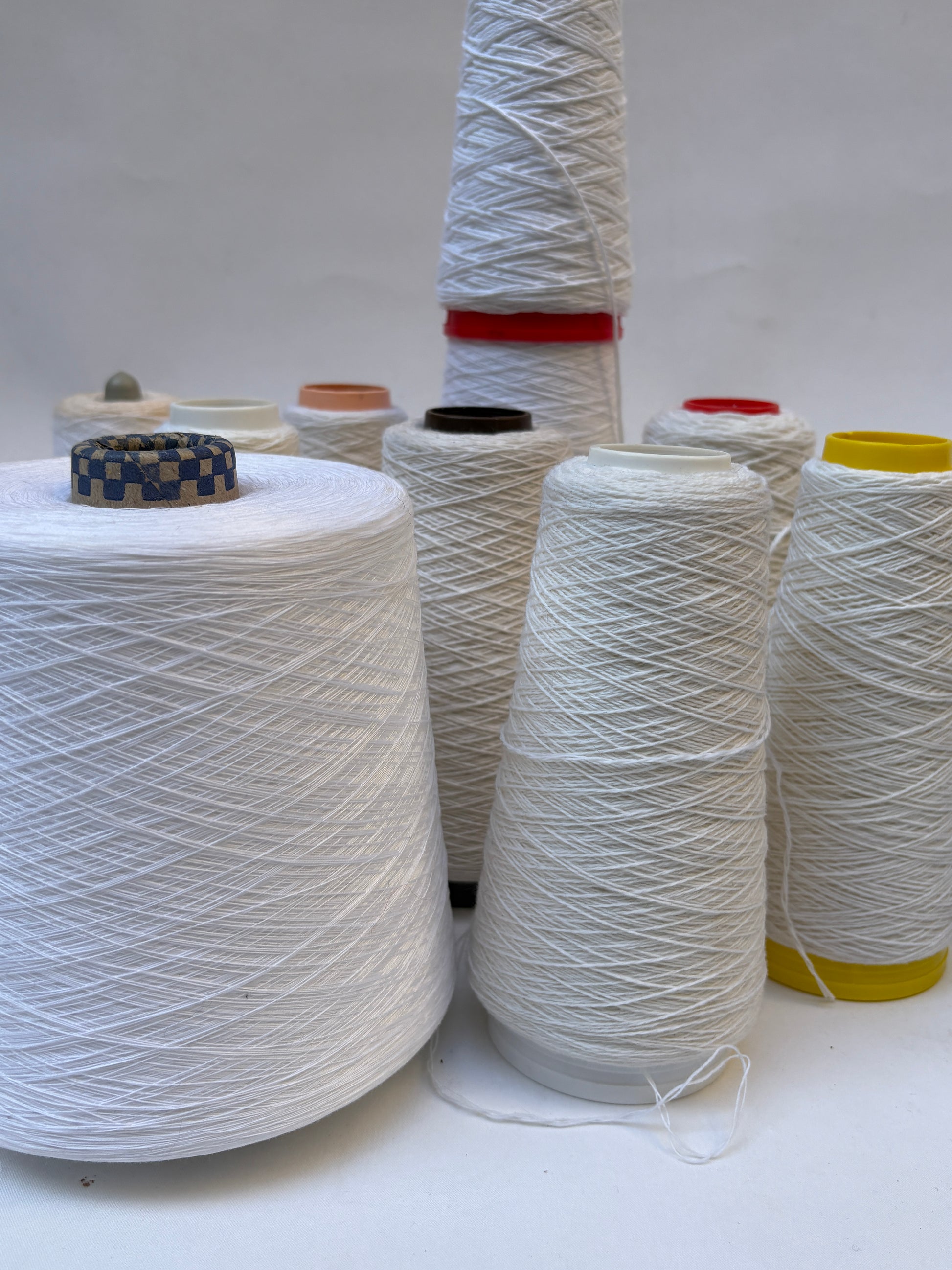 Selection of yarn cones in soft white tones on a white background.