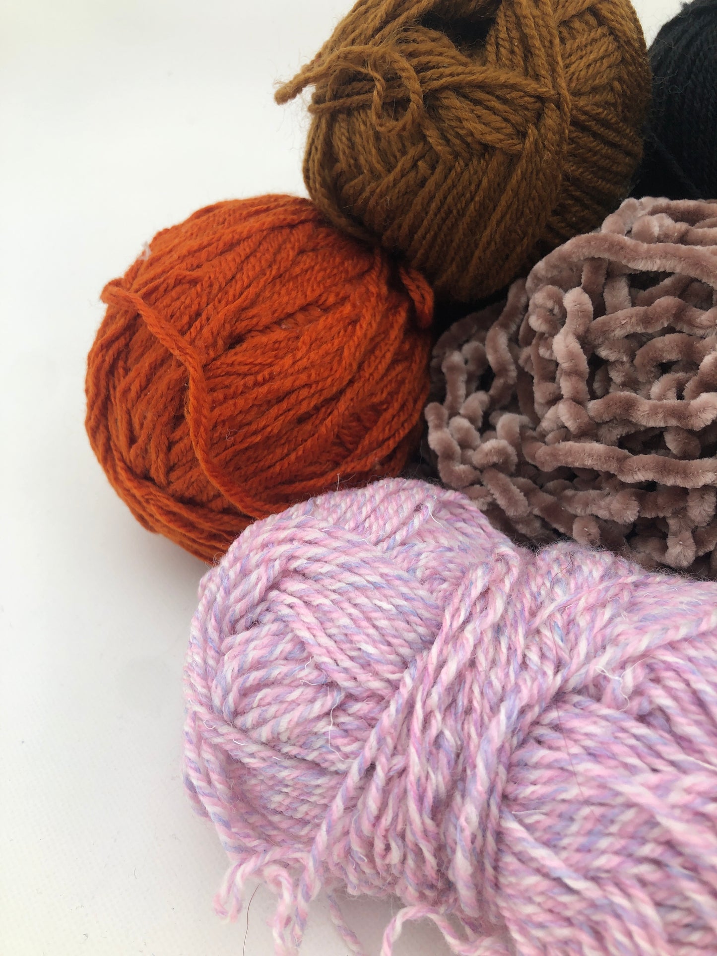 Colourful yarn balls are displayed together on a white surface
